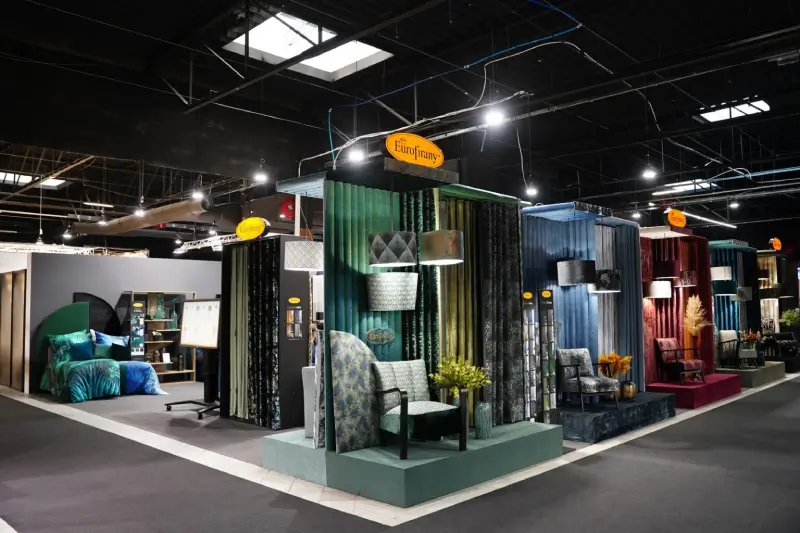 Exhibition stand showcasing interior textiles, fabrics and furniture setups at a trade fair.