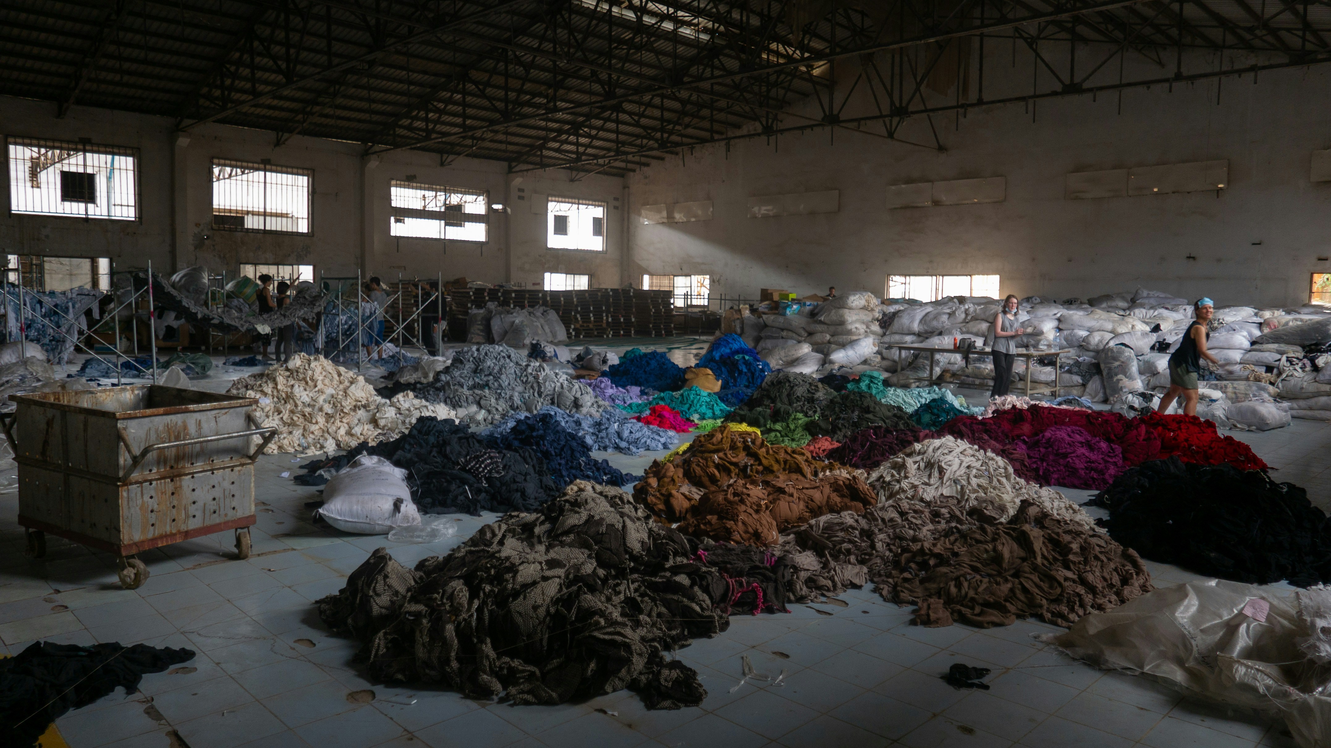 Sorted piles of colourful fabric waste inside a large industrial warehouse.