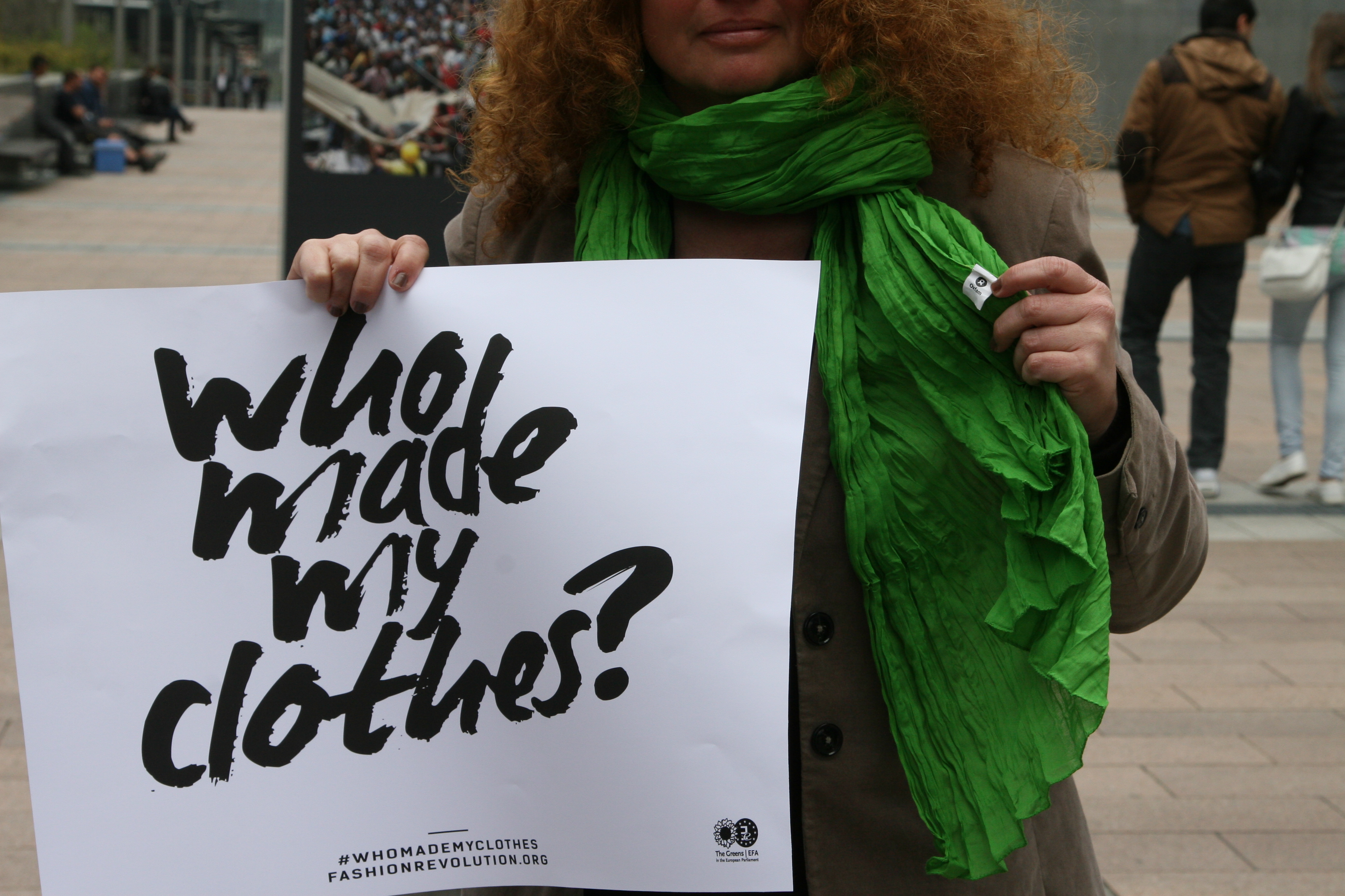 Person holding a sign saying "who made my clothes?"