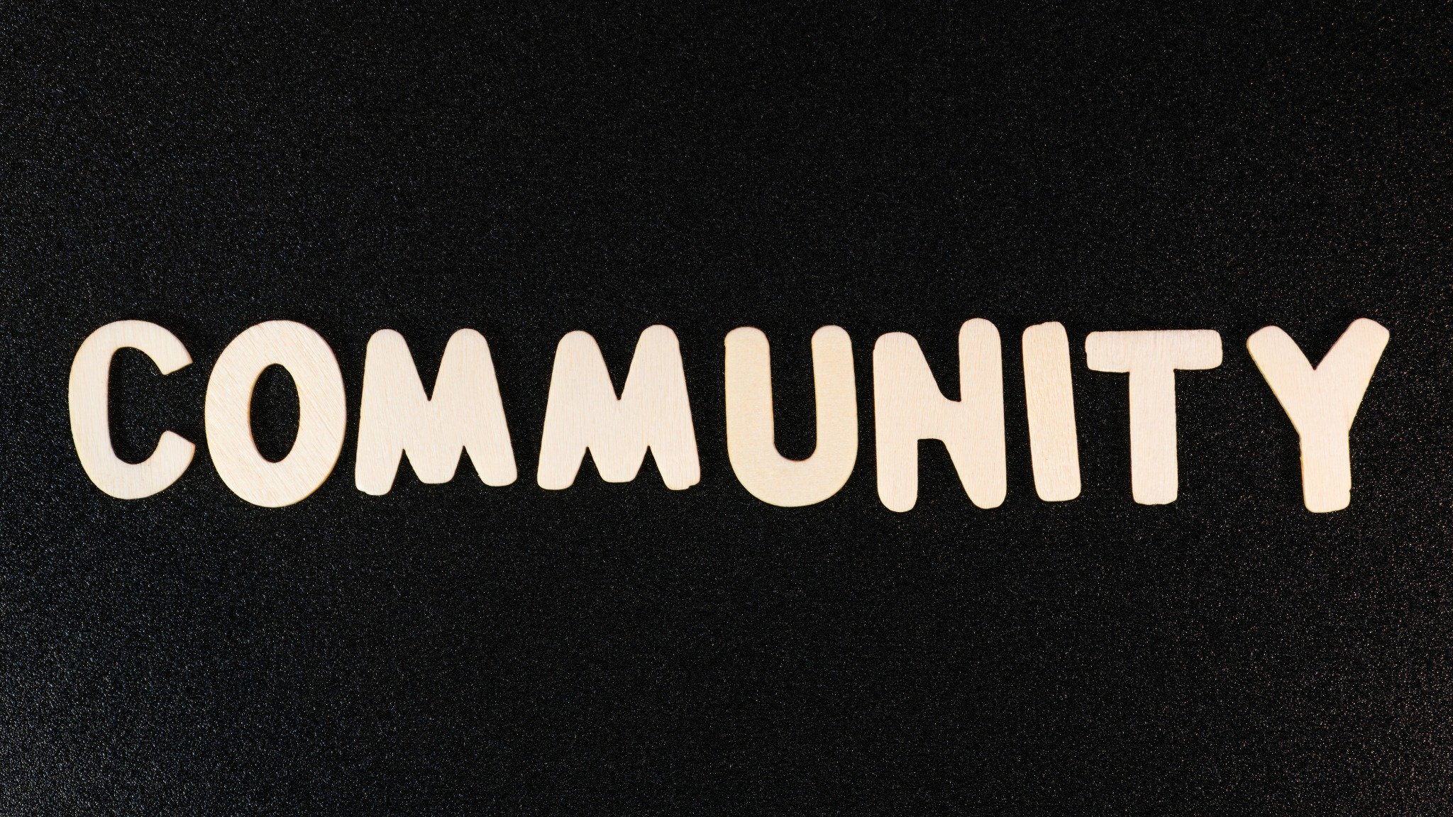Wooden letters spelling “Community” on a dark textured background.