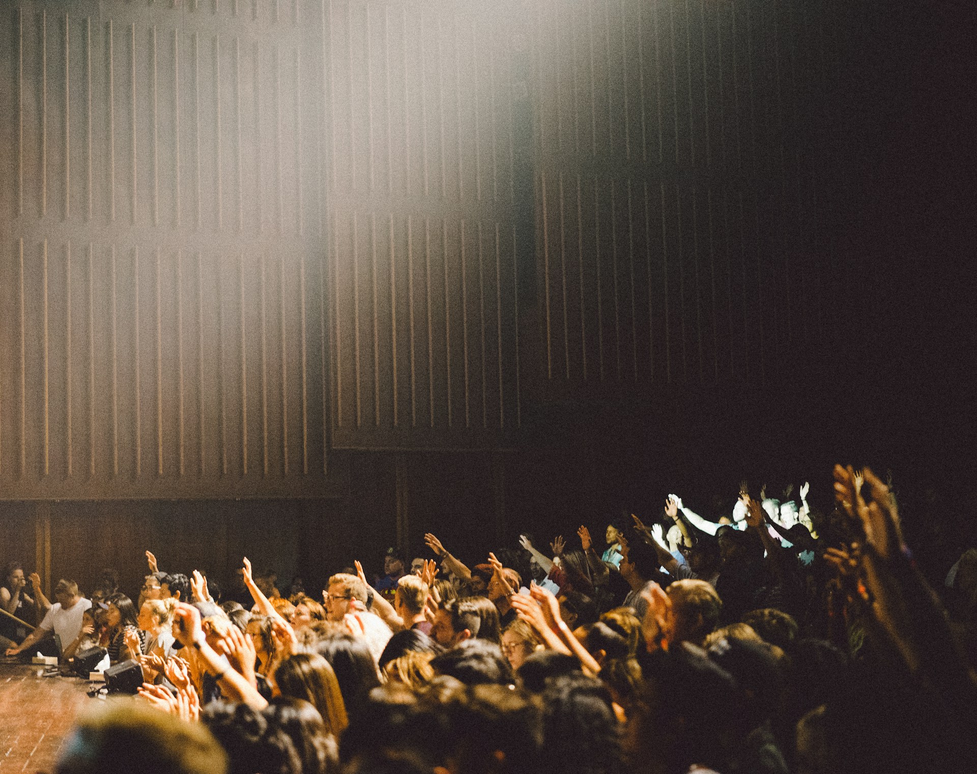 People raising their hands inside auditorium.