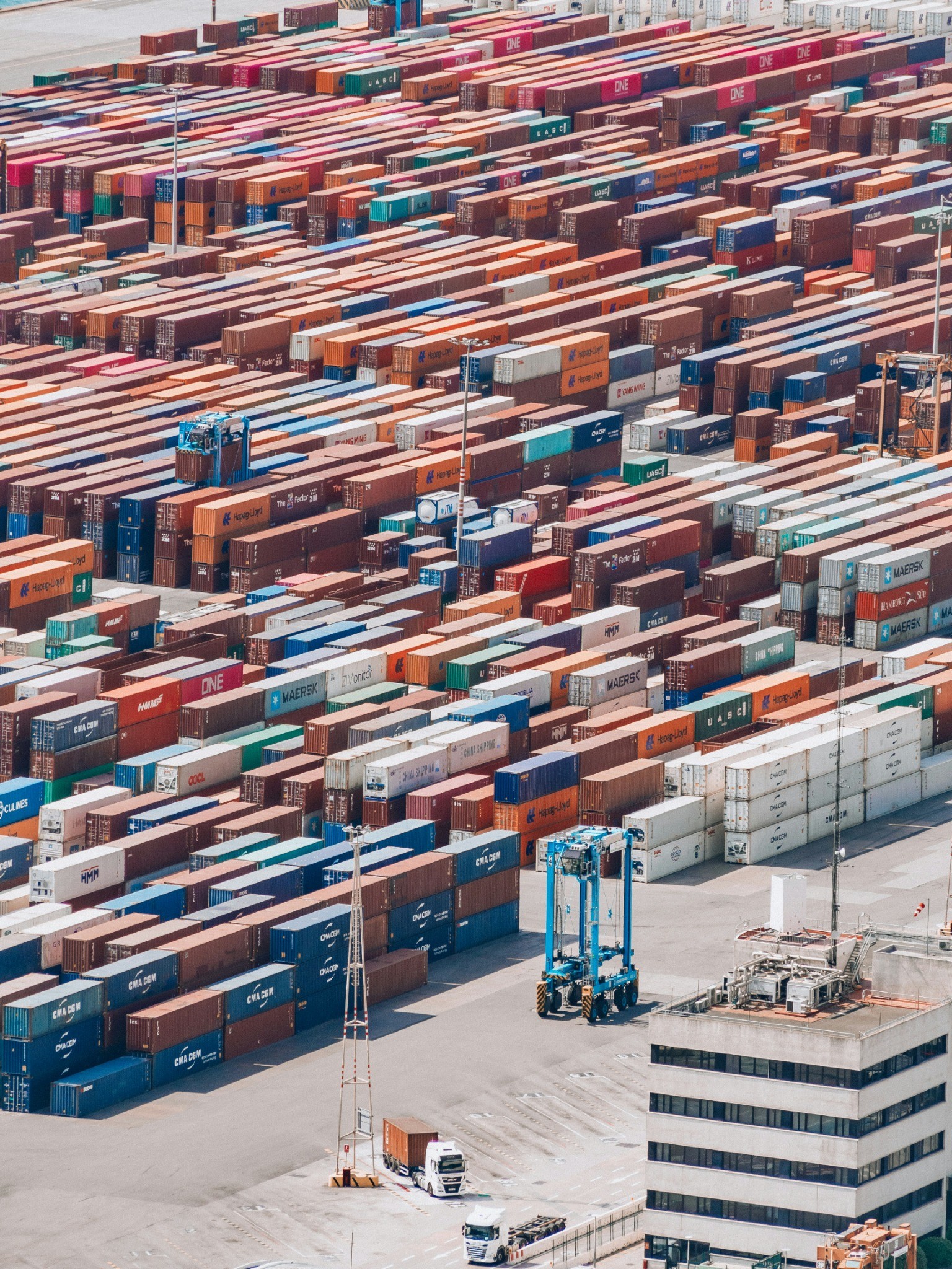 Aerial view of a large container terminal with hundreds of stacked shipping containers and transport vehicles, representing global logistics and international trade.