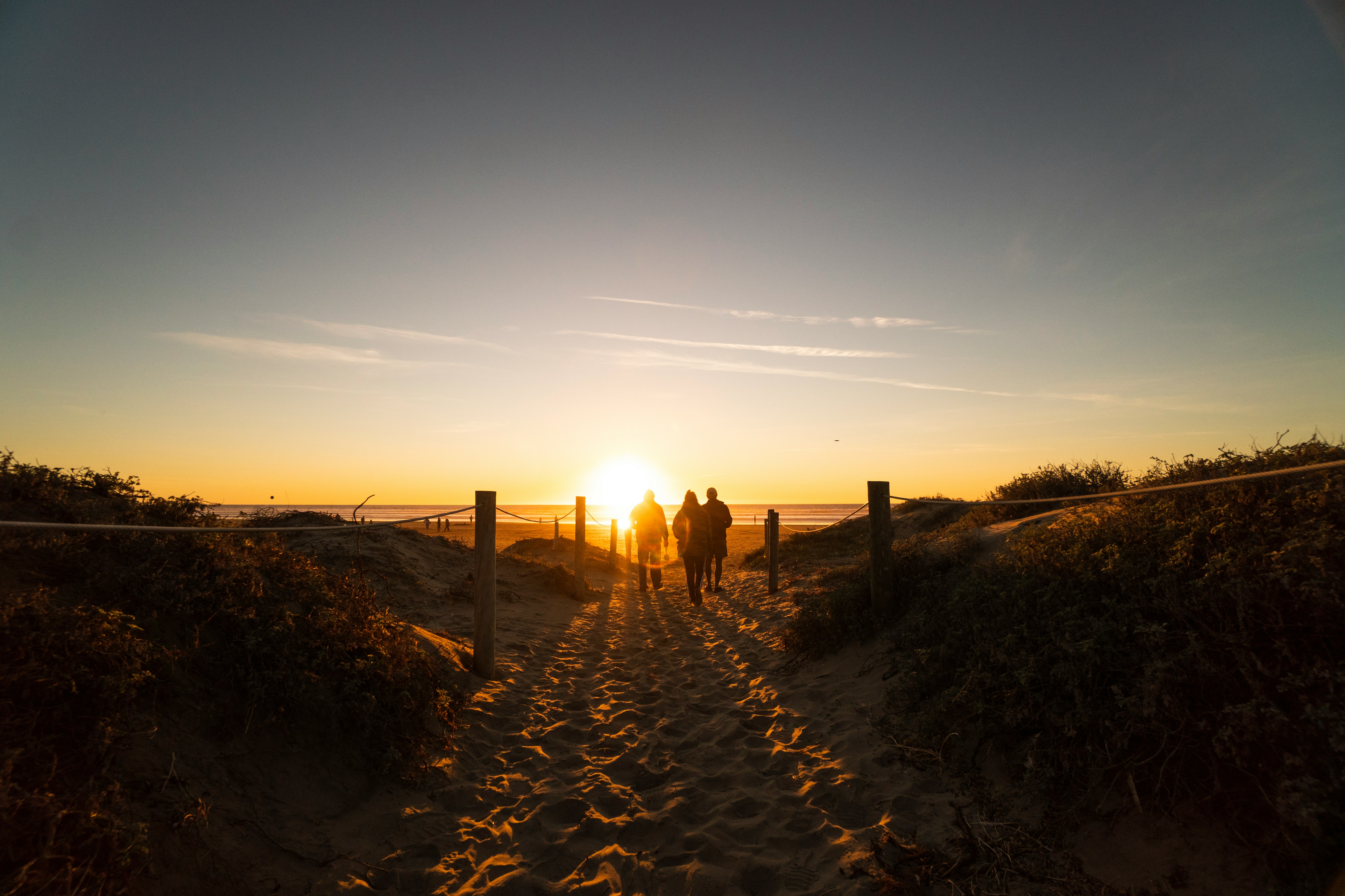 three-person-walking-on-sand-dunes-near-beach
