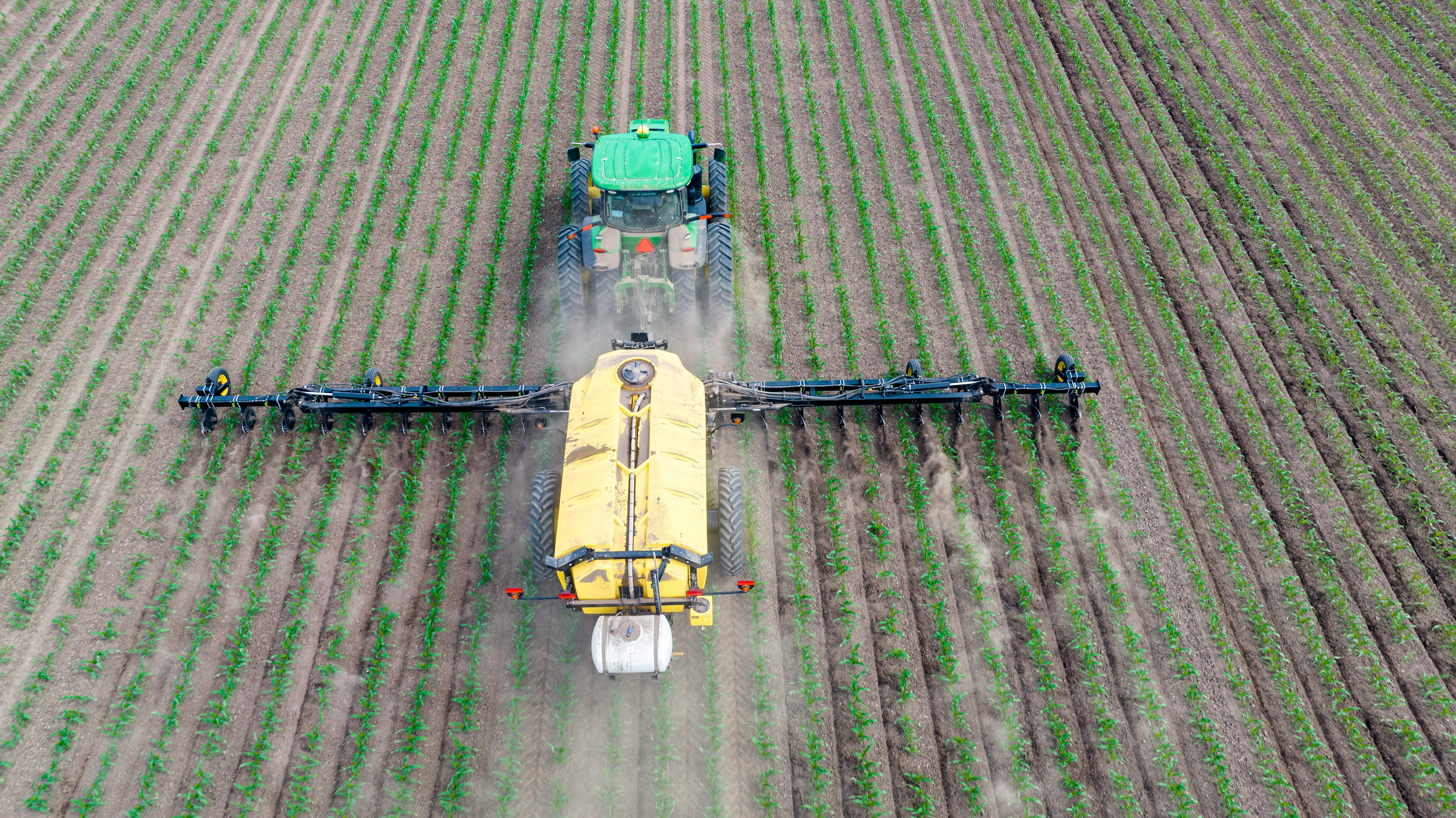 A photo representing a tractor applying fertiliser across a cultivated field.