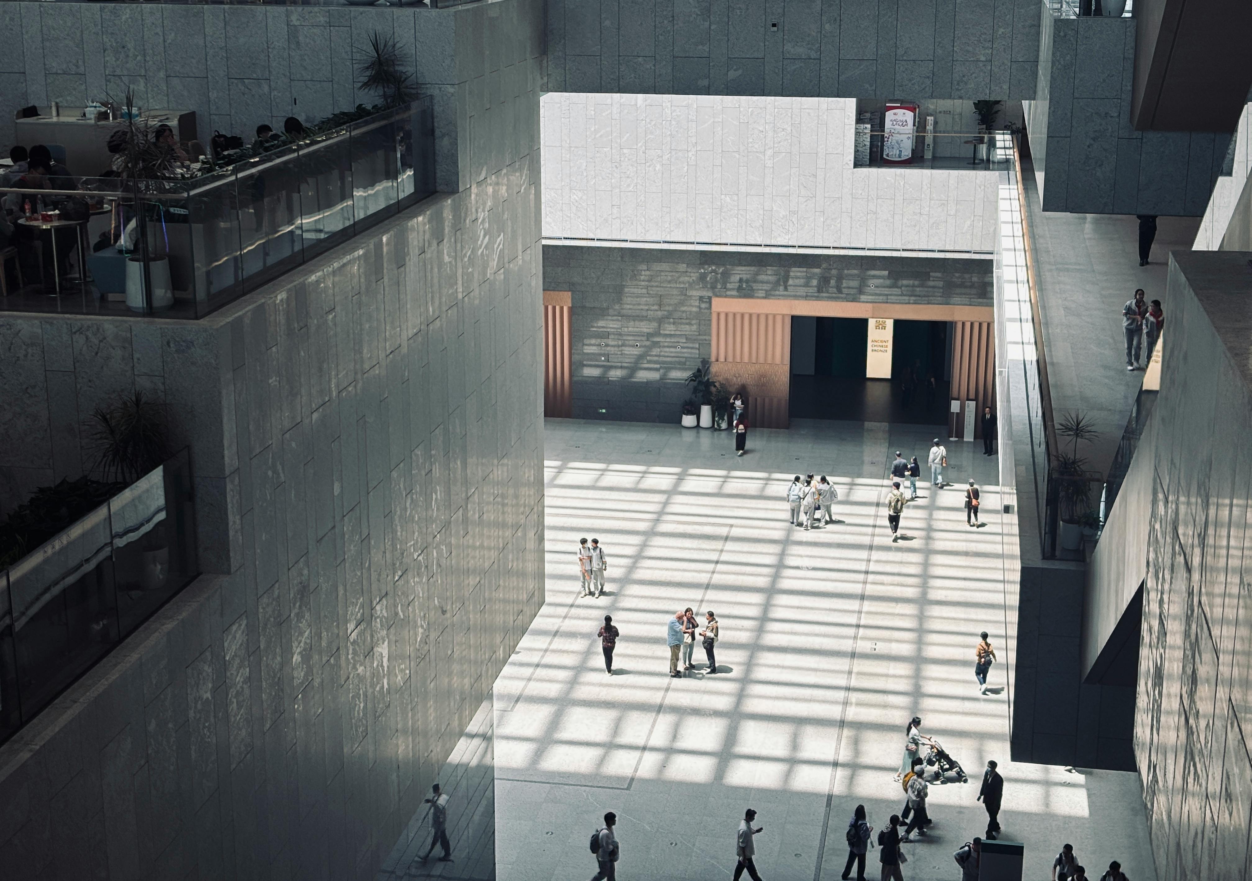 A spacious indoor atrium with geometric shadows and people walking by.