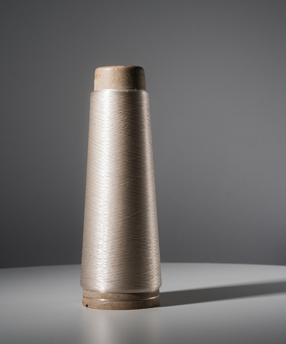 Spool of translucent thread on a cardboard cone with a gray background.