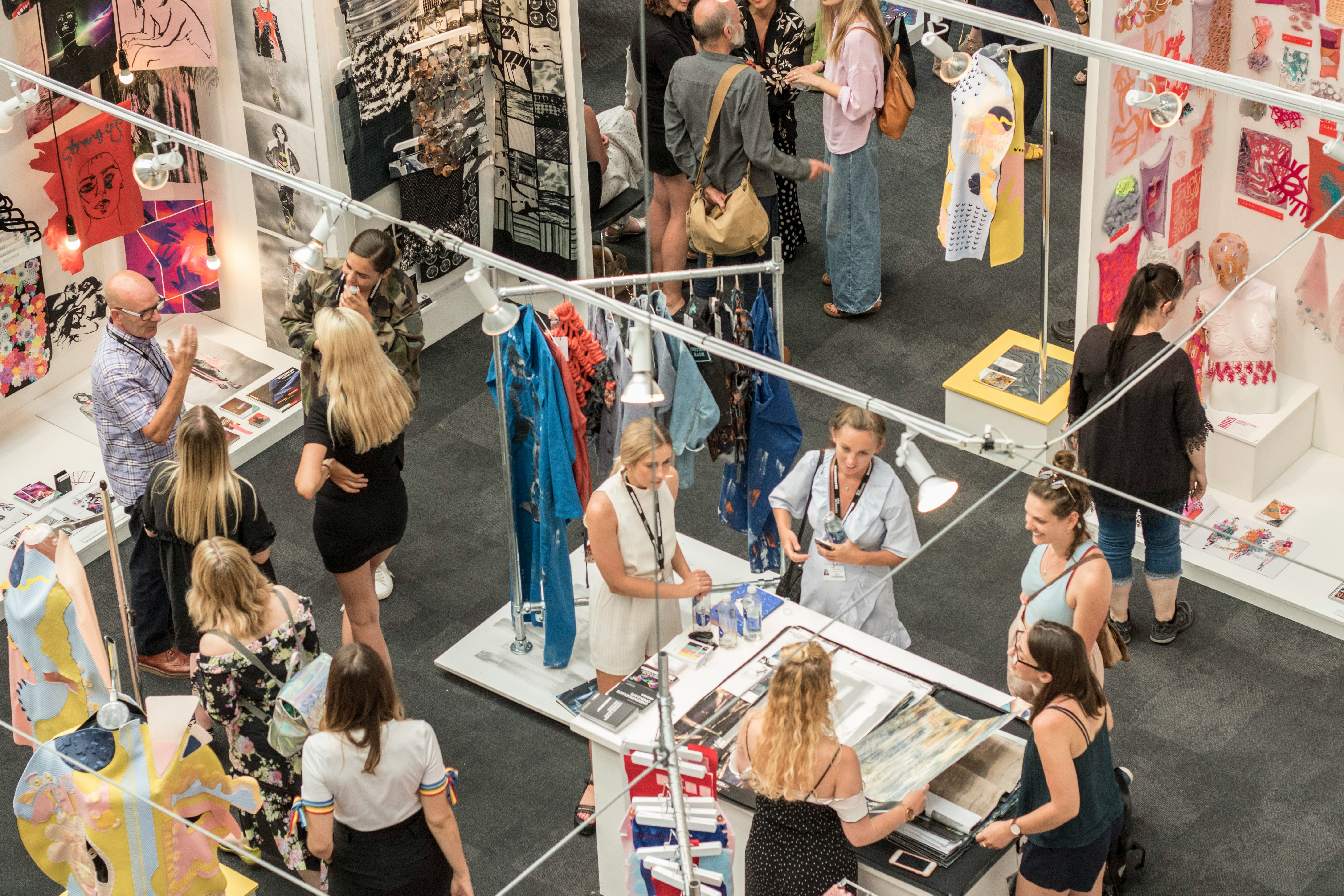 Textile exhibition booth with visitors browsing garments, artwork, and fabric displays.