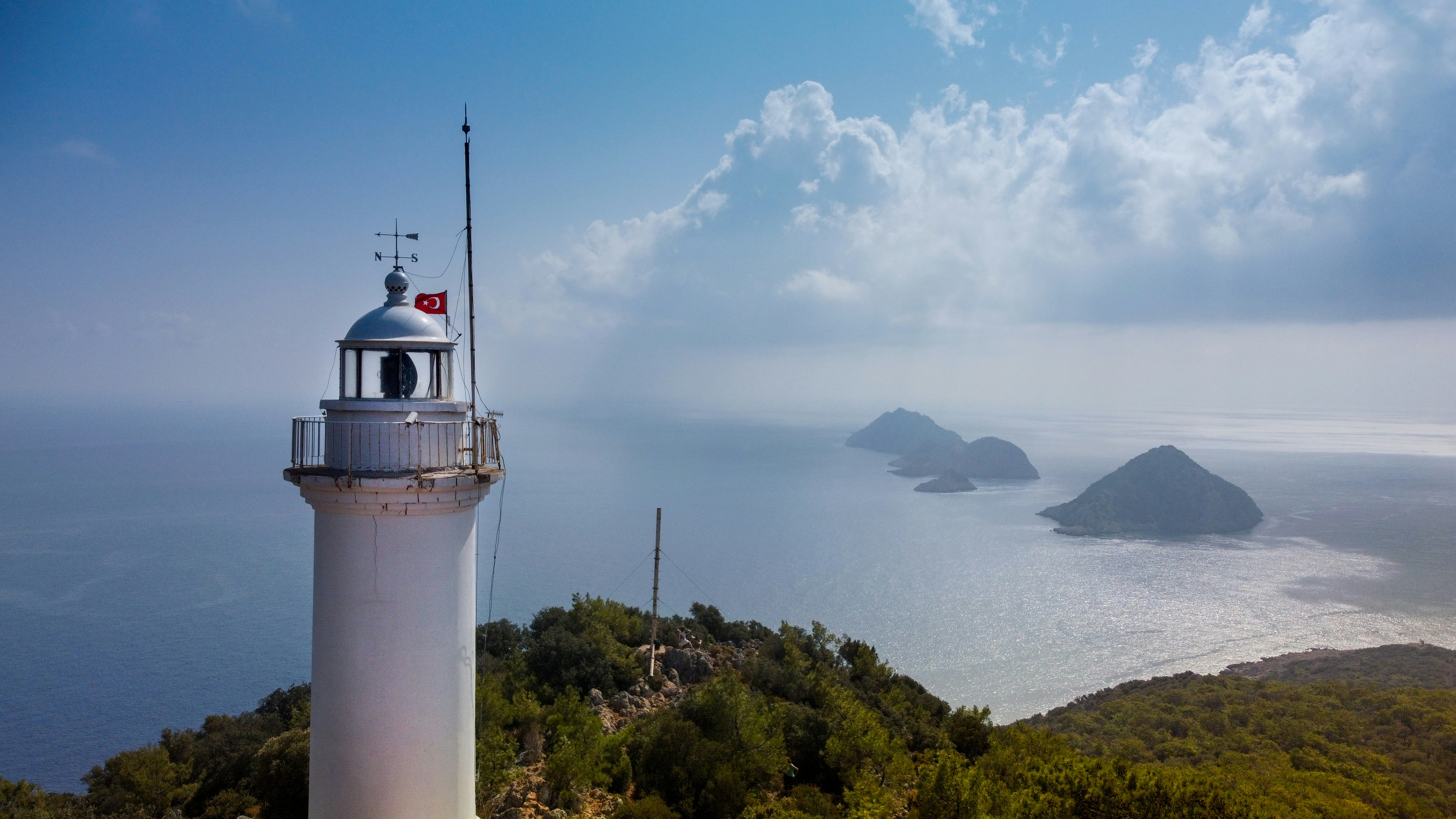 white-and-brown-lighthouse-near-green-trees-under-white-clouds-and-blue-sky