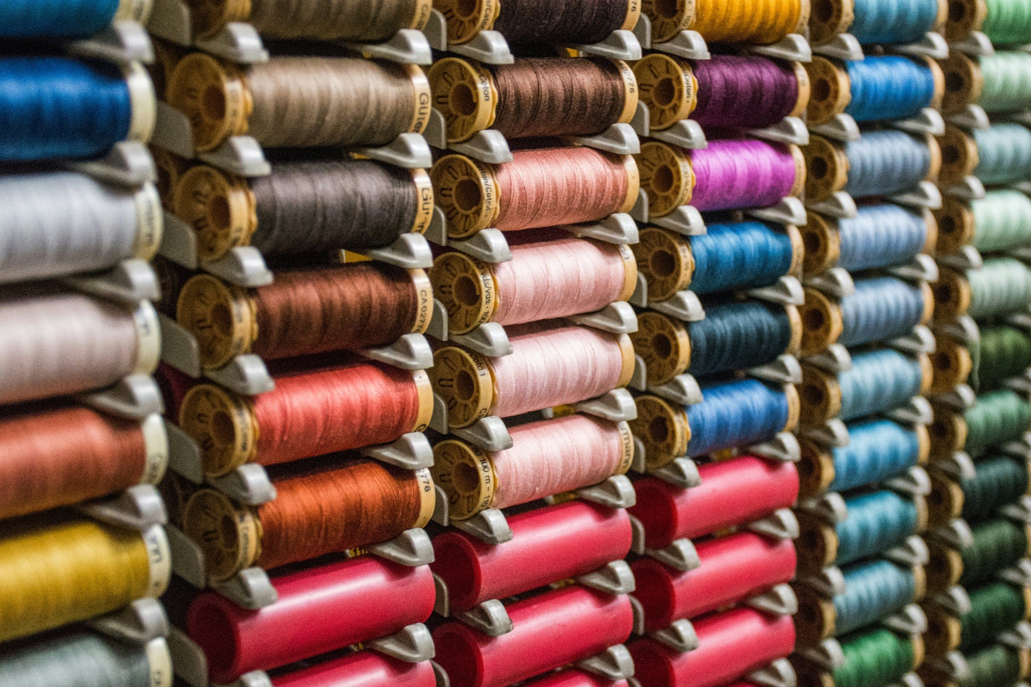 Close up view of multiple colourful thread spools arranged on shelves, representing textile manufacturing, yarn production and material diversity within the textile industry.