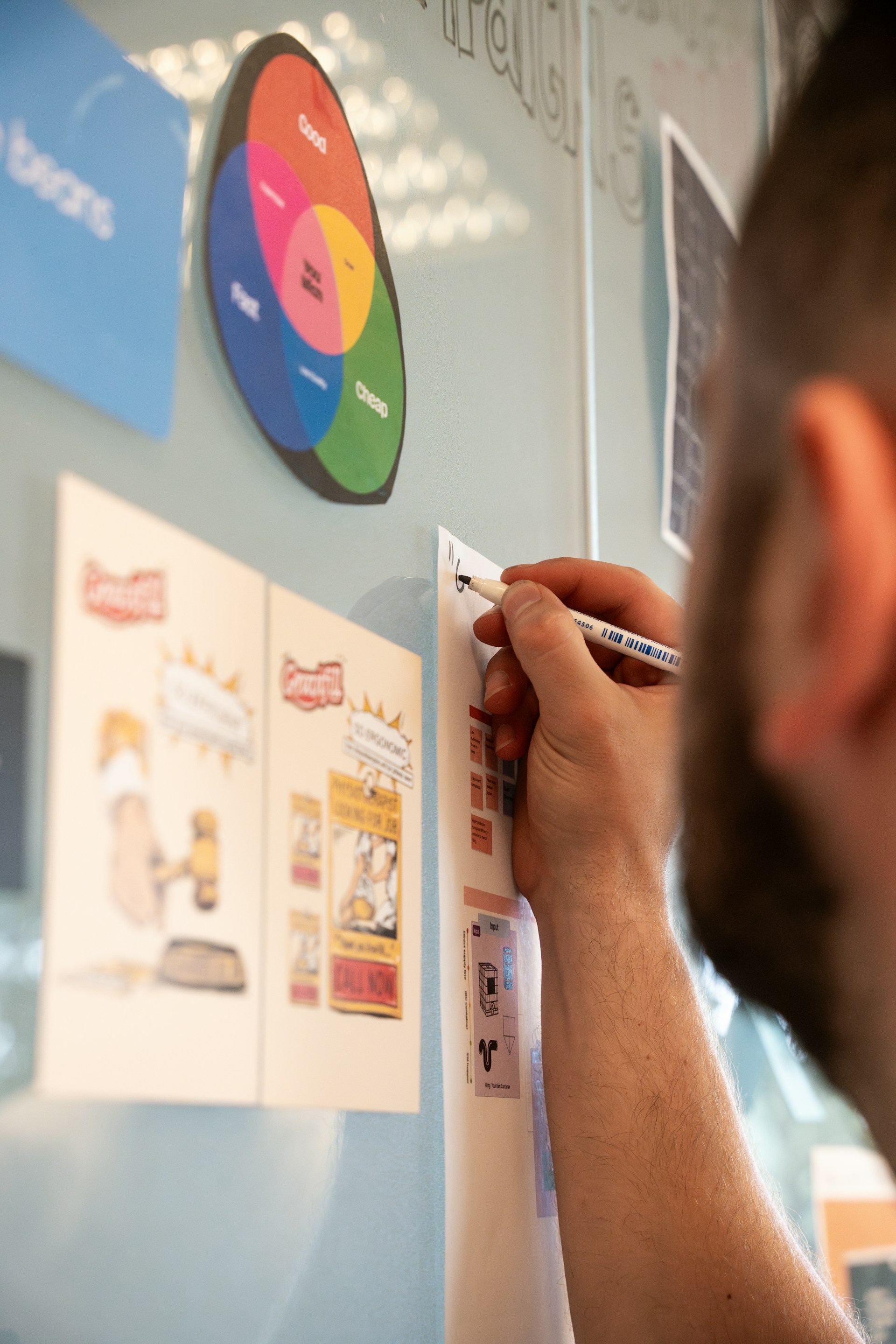 Person writing notes on a wall with diagrams and printed materials.