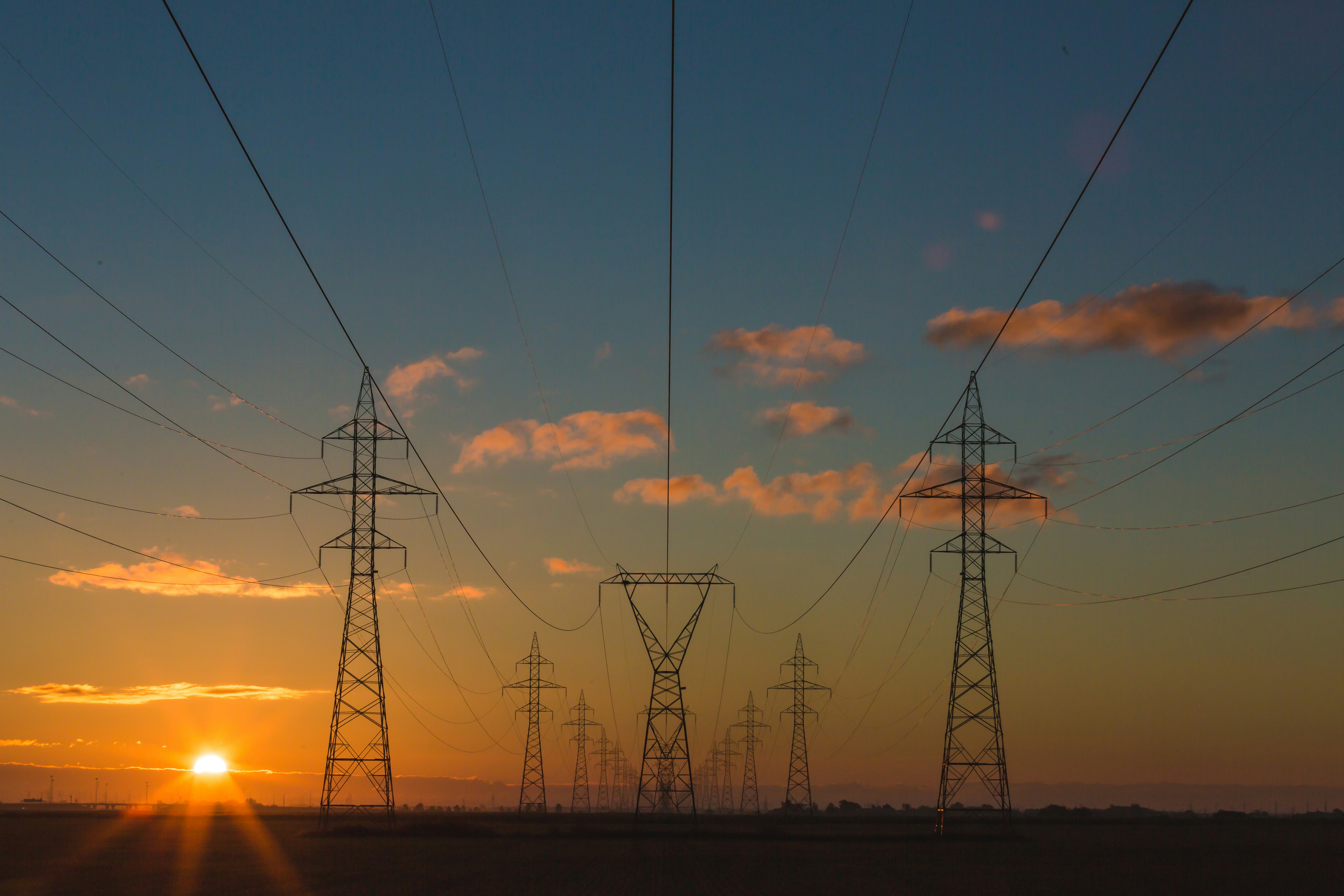 A graphic presenting high-voltage power lines stretch across an open landscape at sunset.
