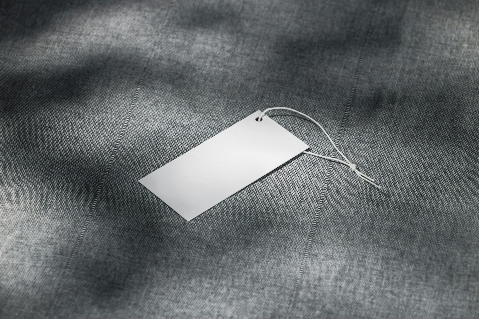 Blank clothing tag resting on a grey textile fabric surface.