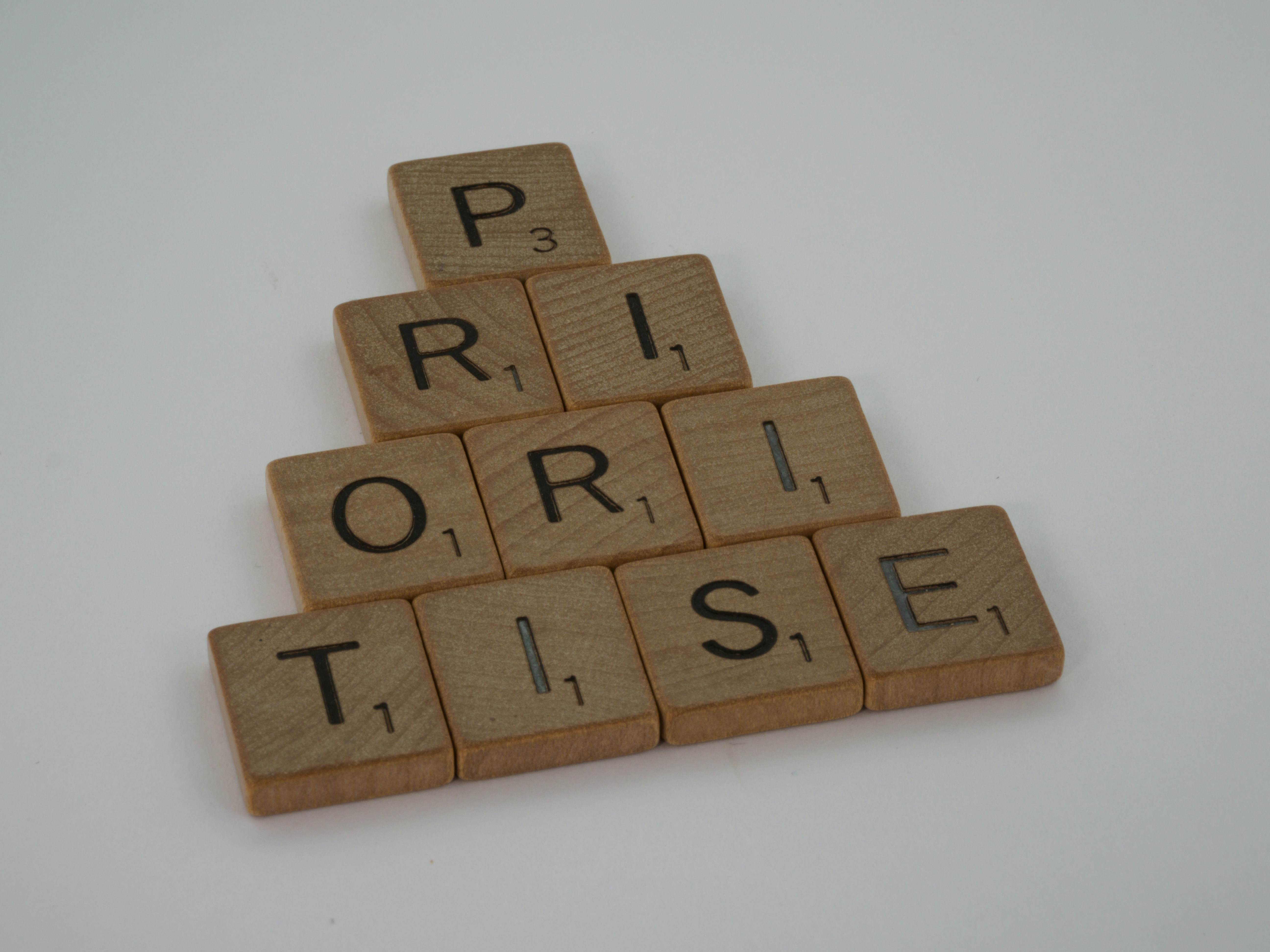 A photo presenting wooden letter tiles arranged in a pyramid to spell "prioritise".