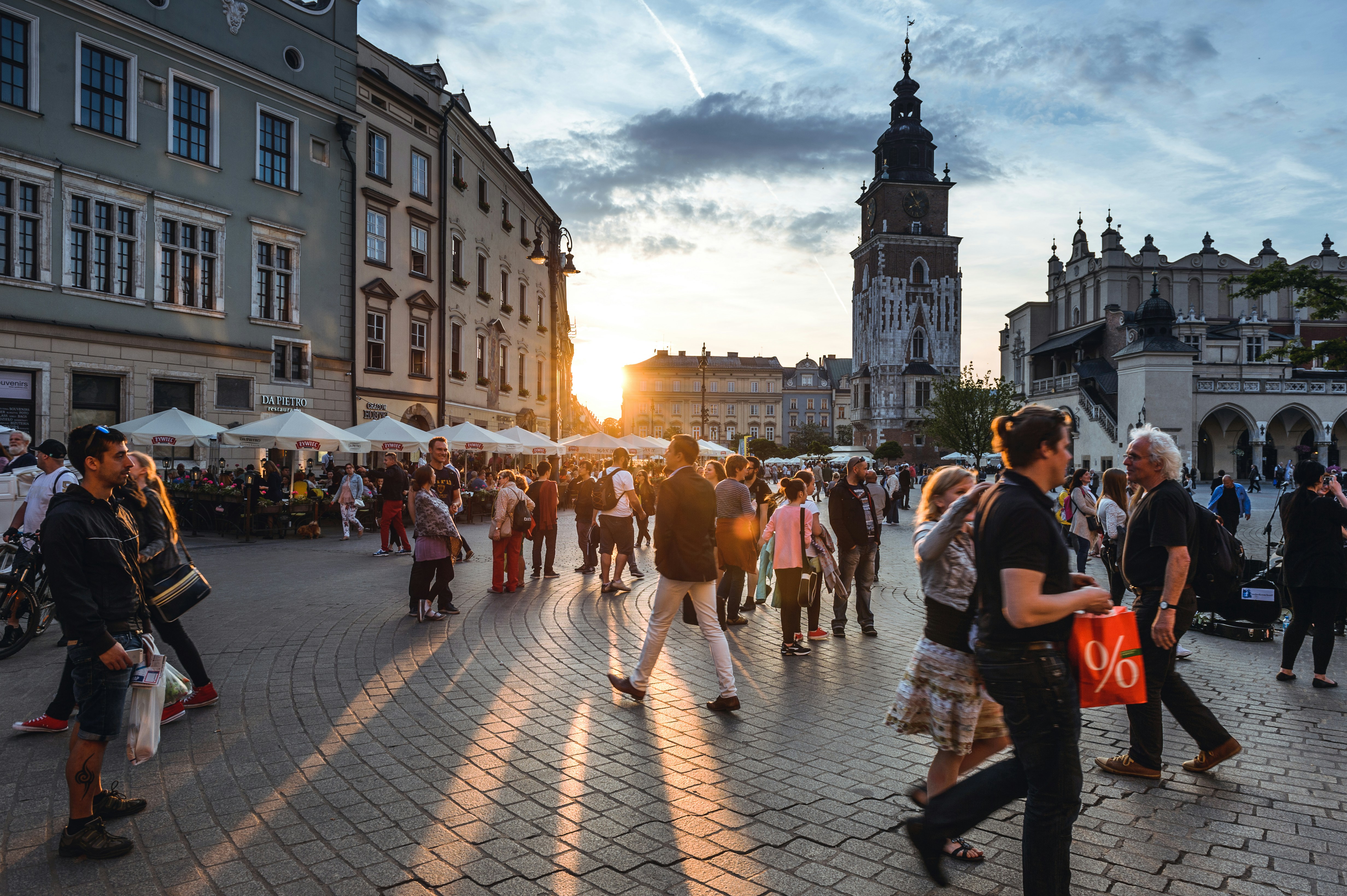 A picture presents people walking through a busy city square at sunset.