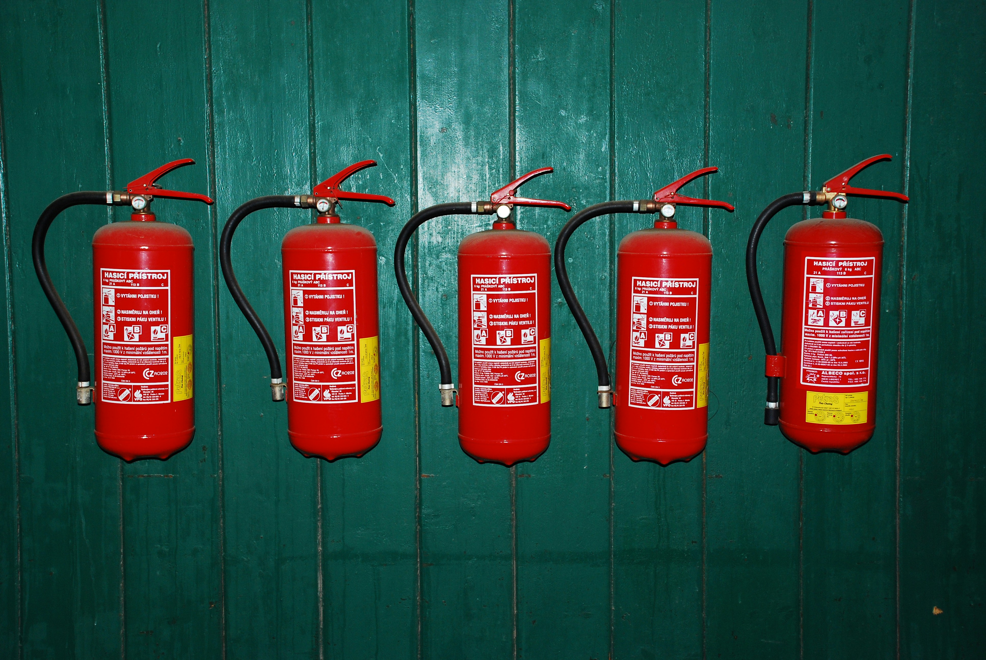 A photo presents fire extinguishers mounted on a green wall.