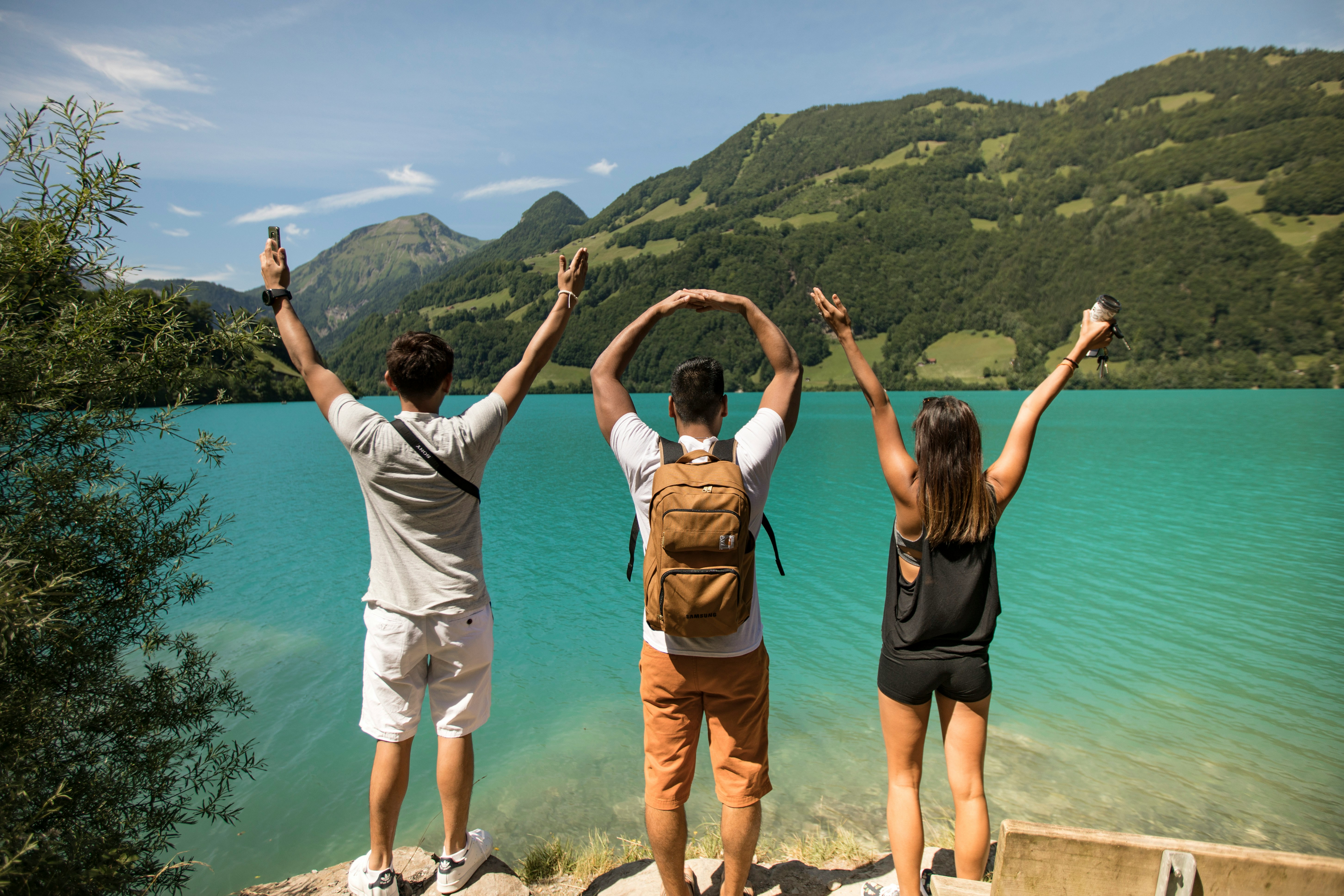 A picture presents three people enjoying a lake and mountain view.