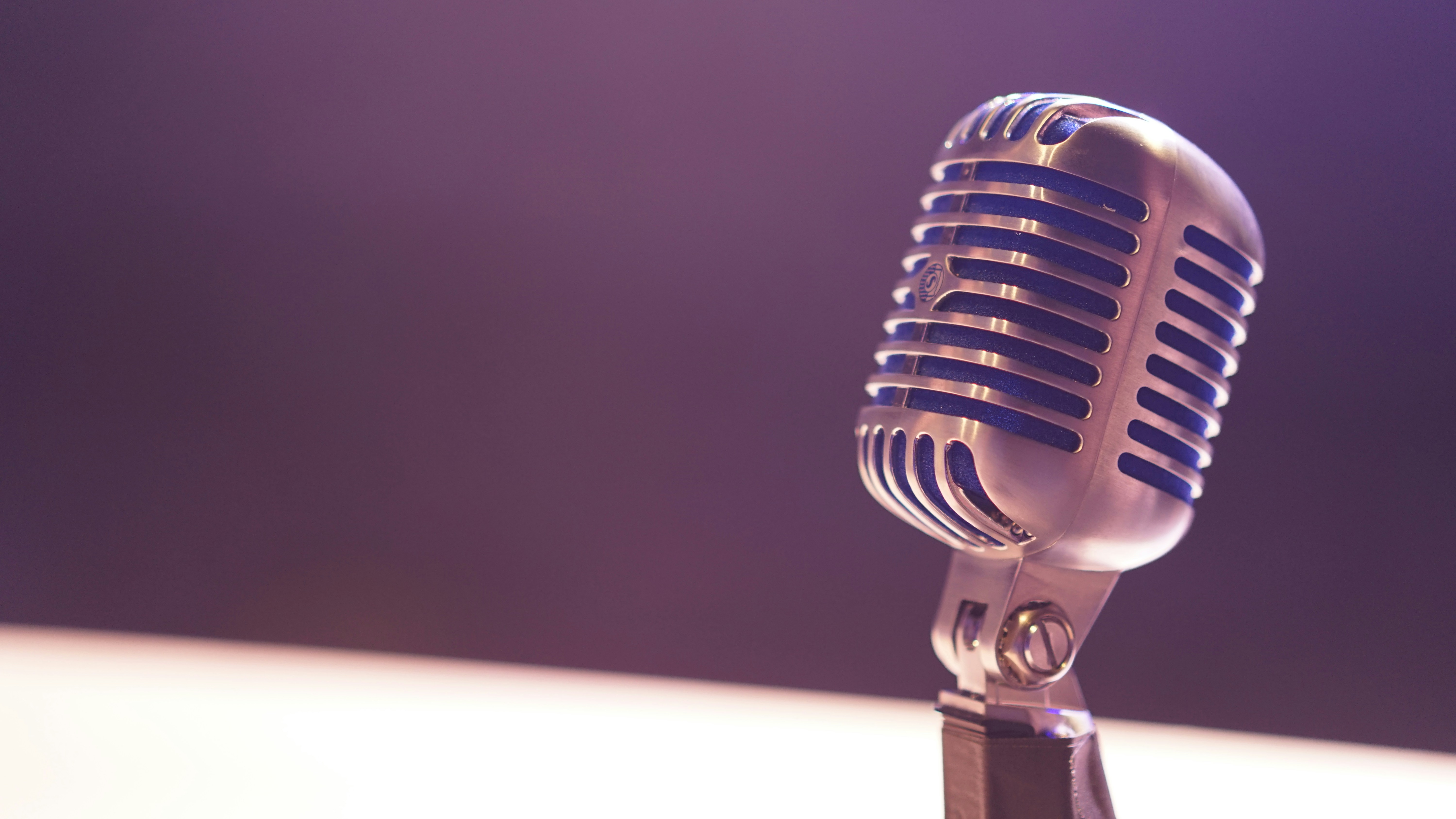 Photo presenting a vintage microphone on a stand against a blurred purple background.