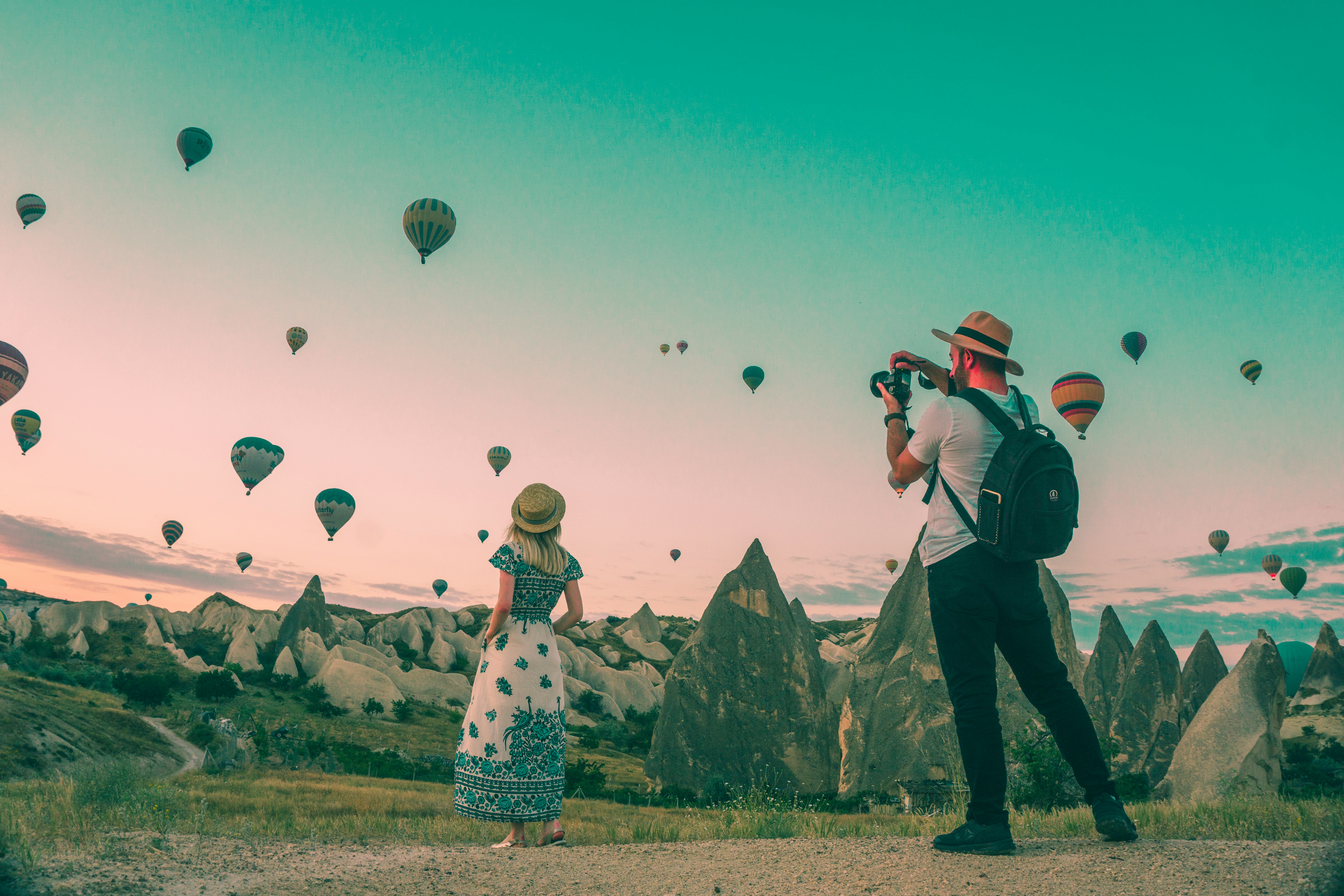 A photo of two tourists watching hot air balloons over a rocky landscape.