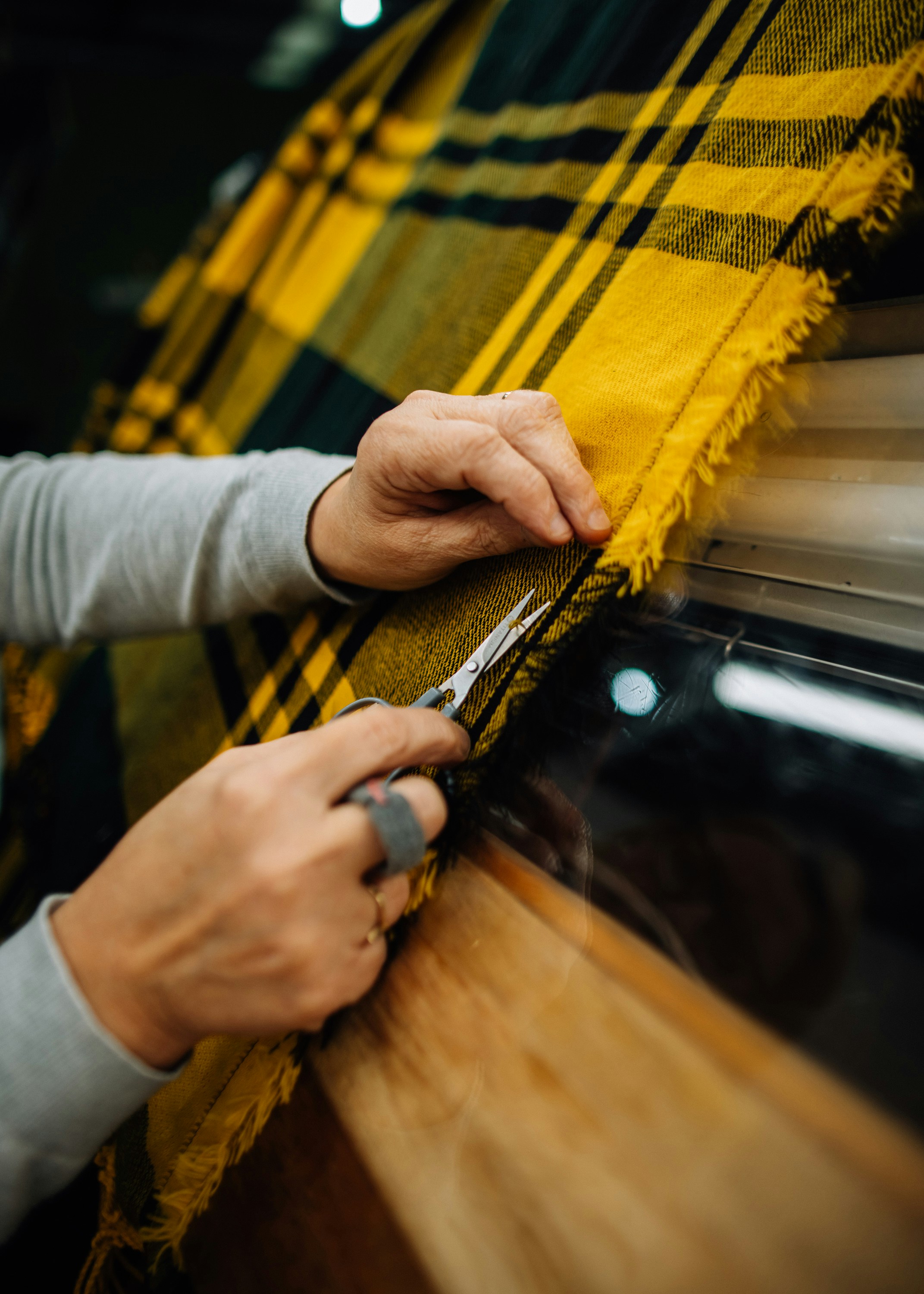 Close up of hands inspecting and trimming a woven textile fabric, demonstrating textile quality control, craftsmanship and material evaluation during fabric production.
