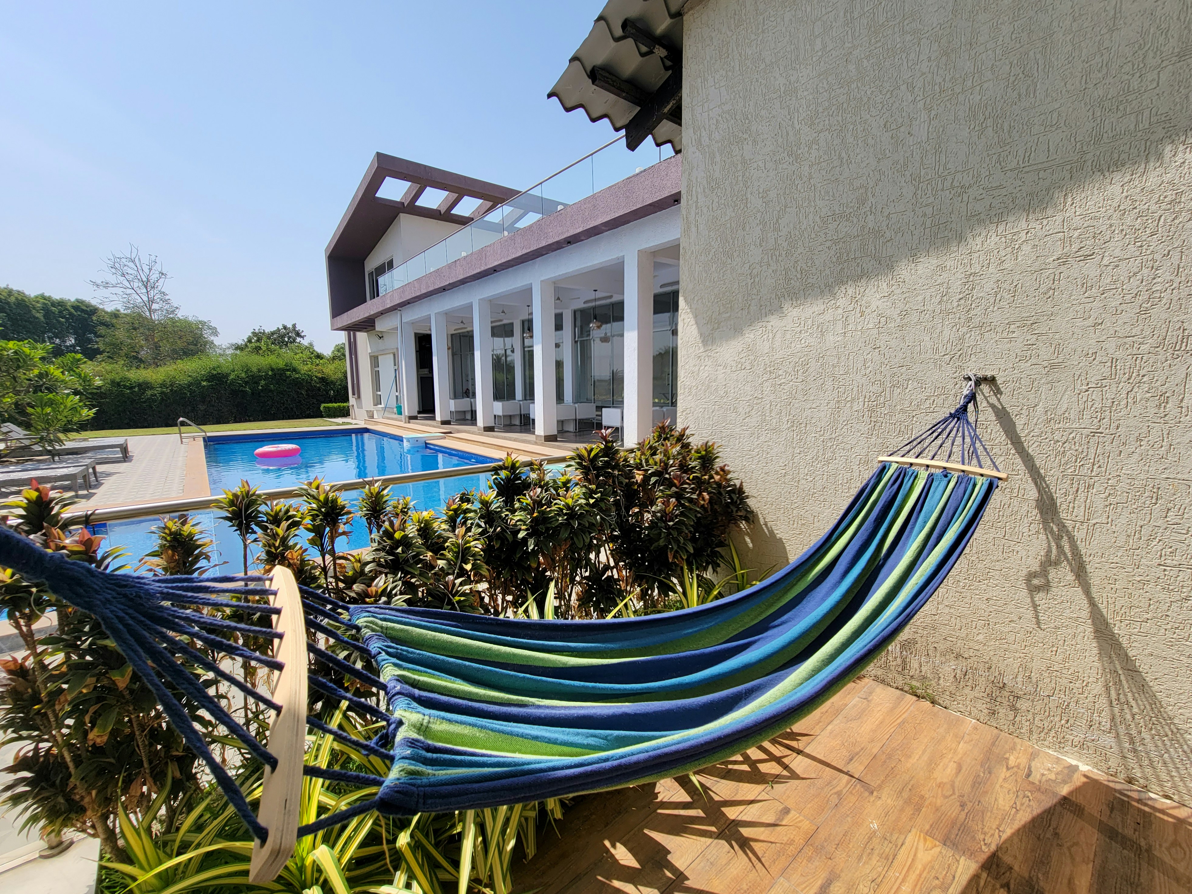 The picture presents a colorful hammock beside a swimming pool at a modern house.