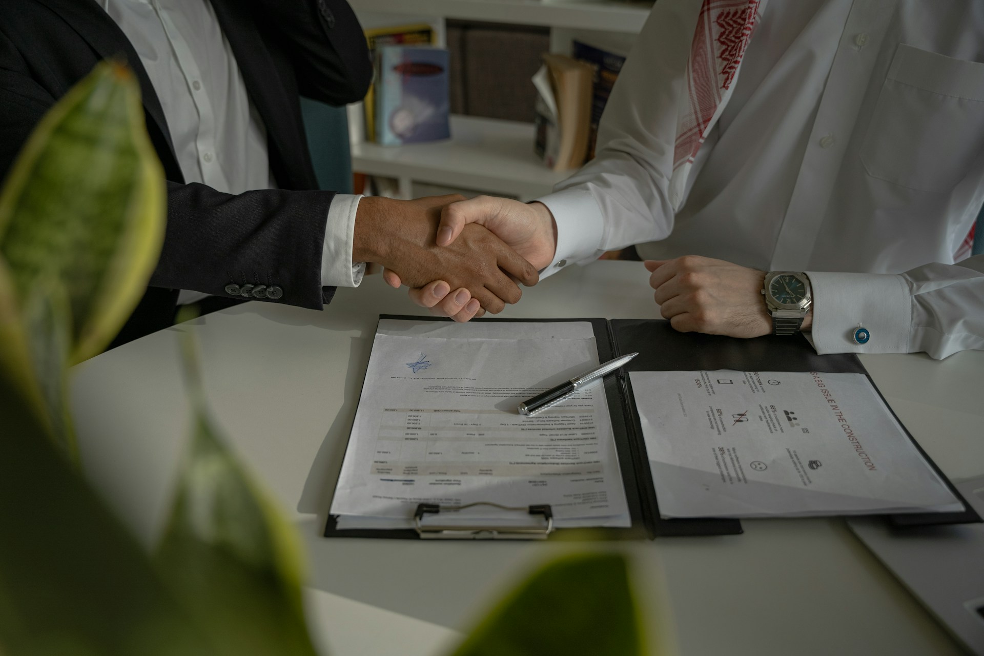 The photo presents two businesspeople shaking hands over signed documents, symbolising an agreement or partnership.