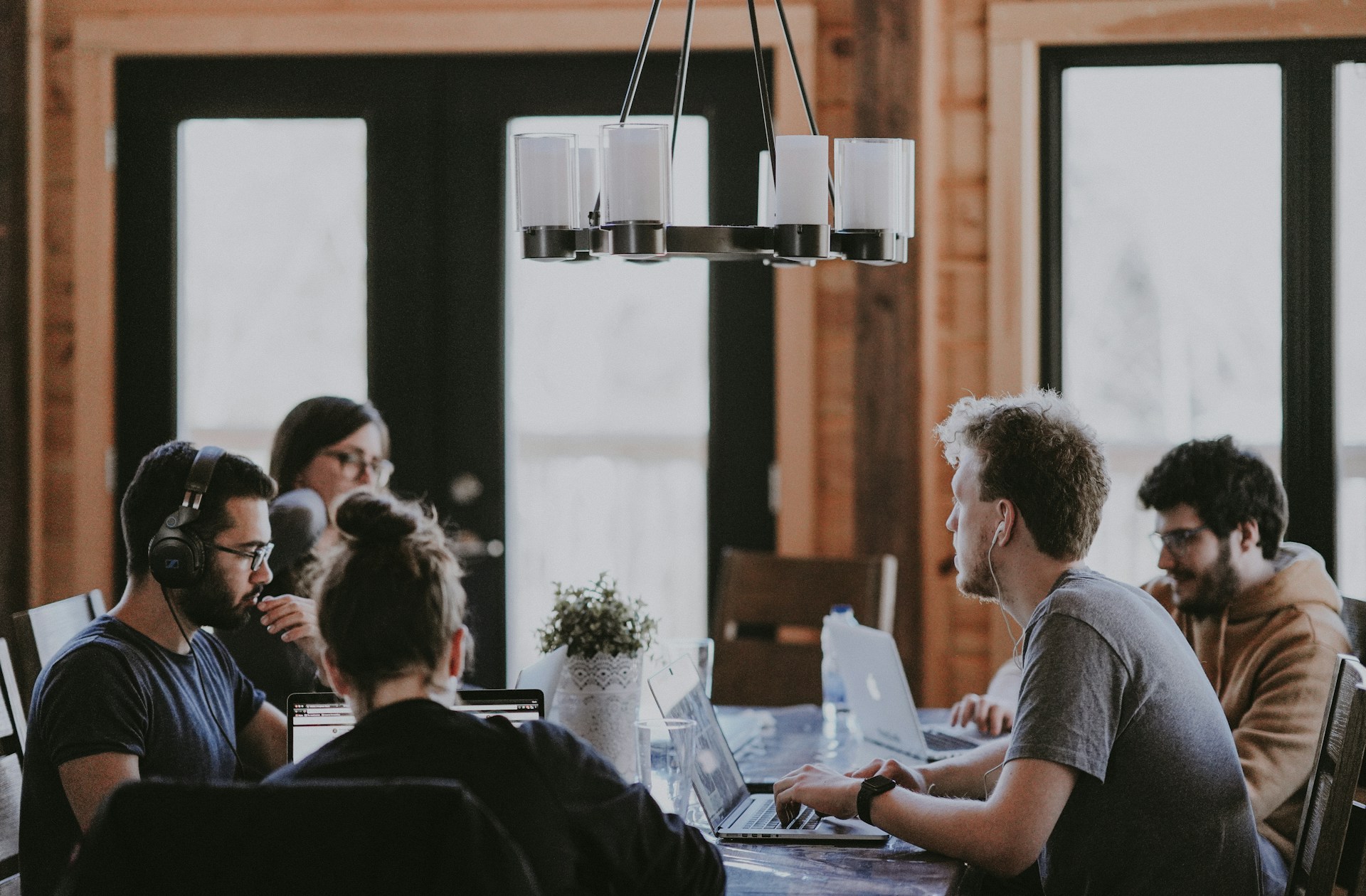 The photo presents a group of people working together with laptops around a table in a collaborative office environment.