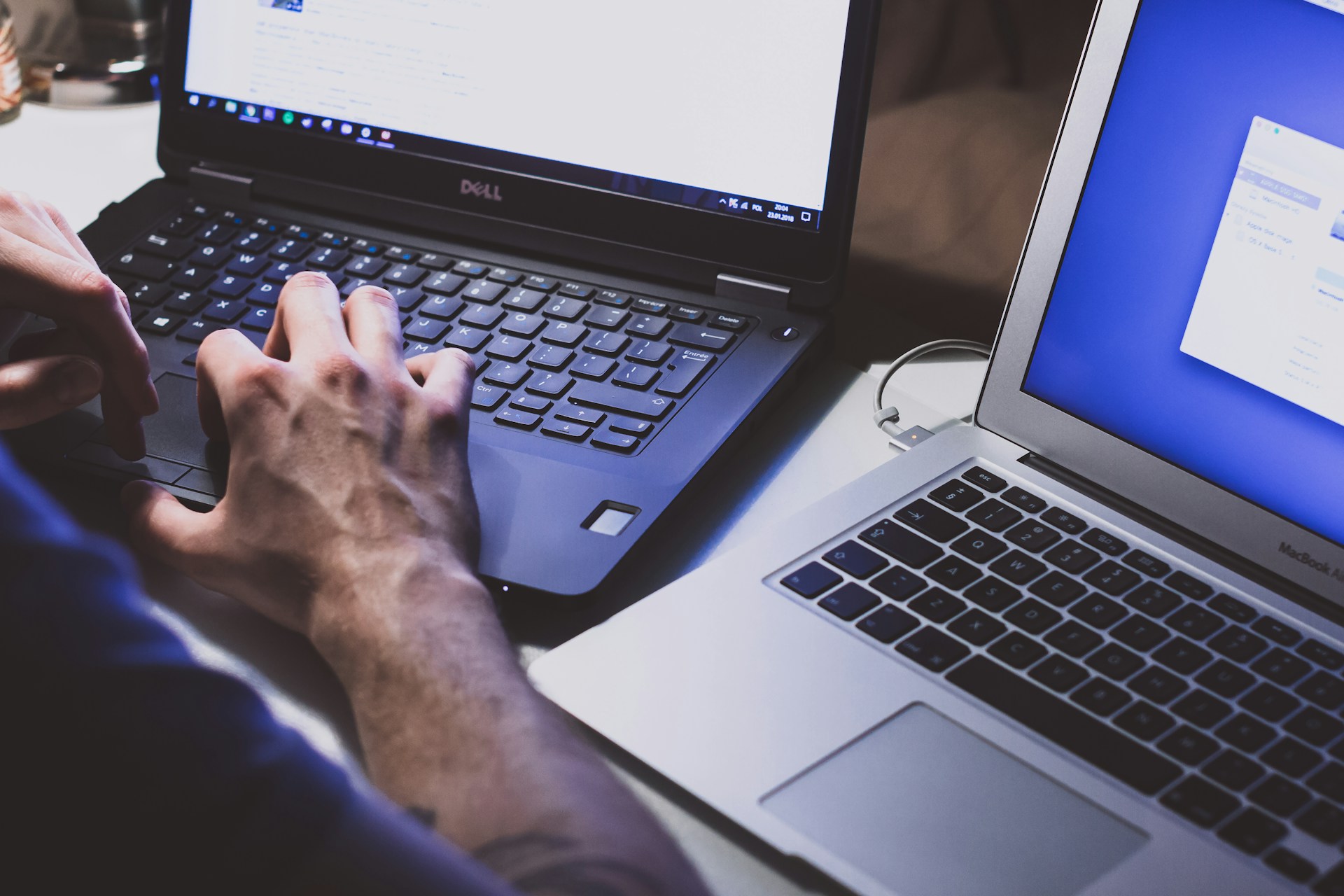 The photo presents a person working on two laptops.