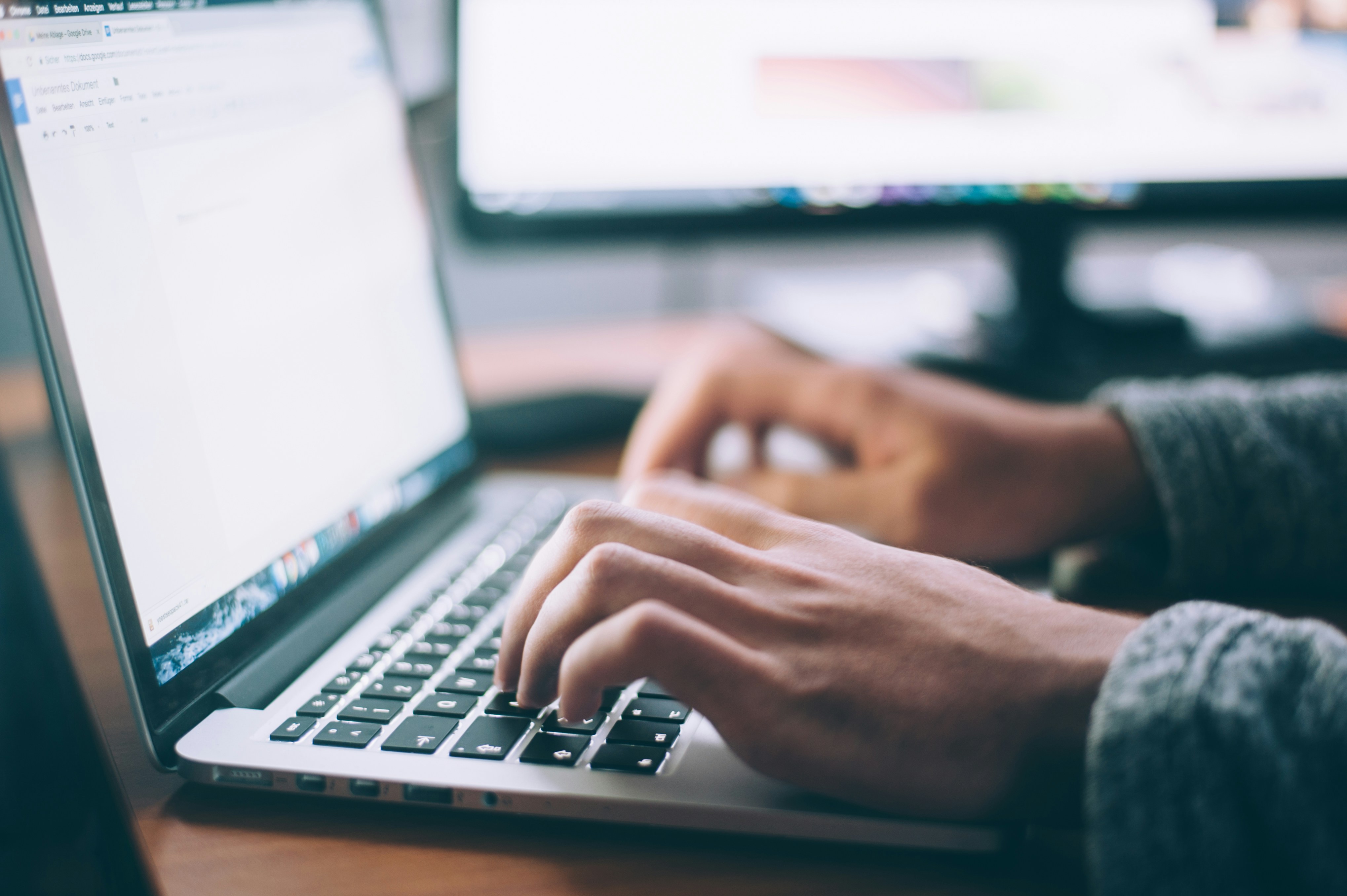 The photo presents a person typing on a laptop.