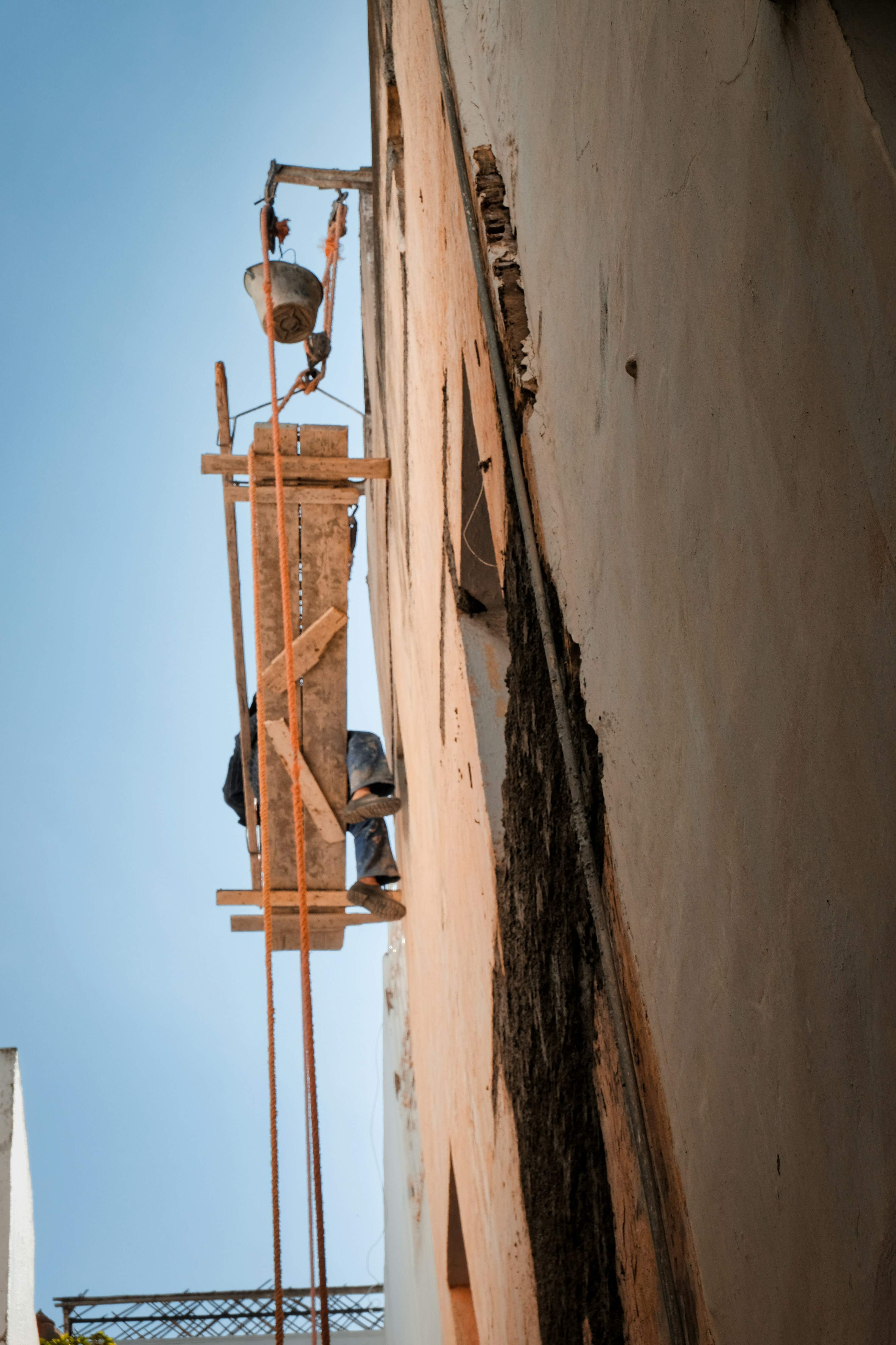 The picture presents a worker on a suspended scaffold beside a tall building wall.