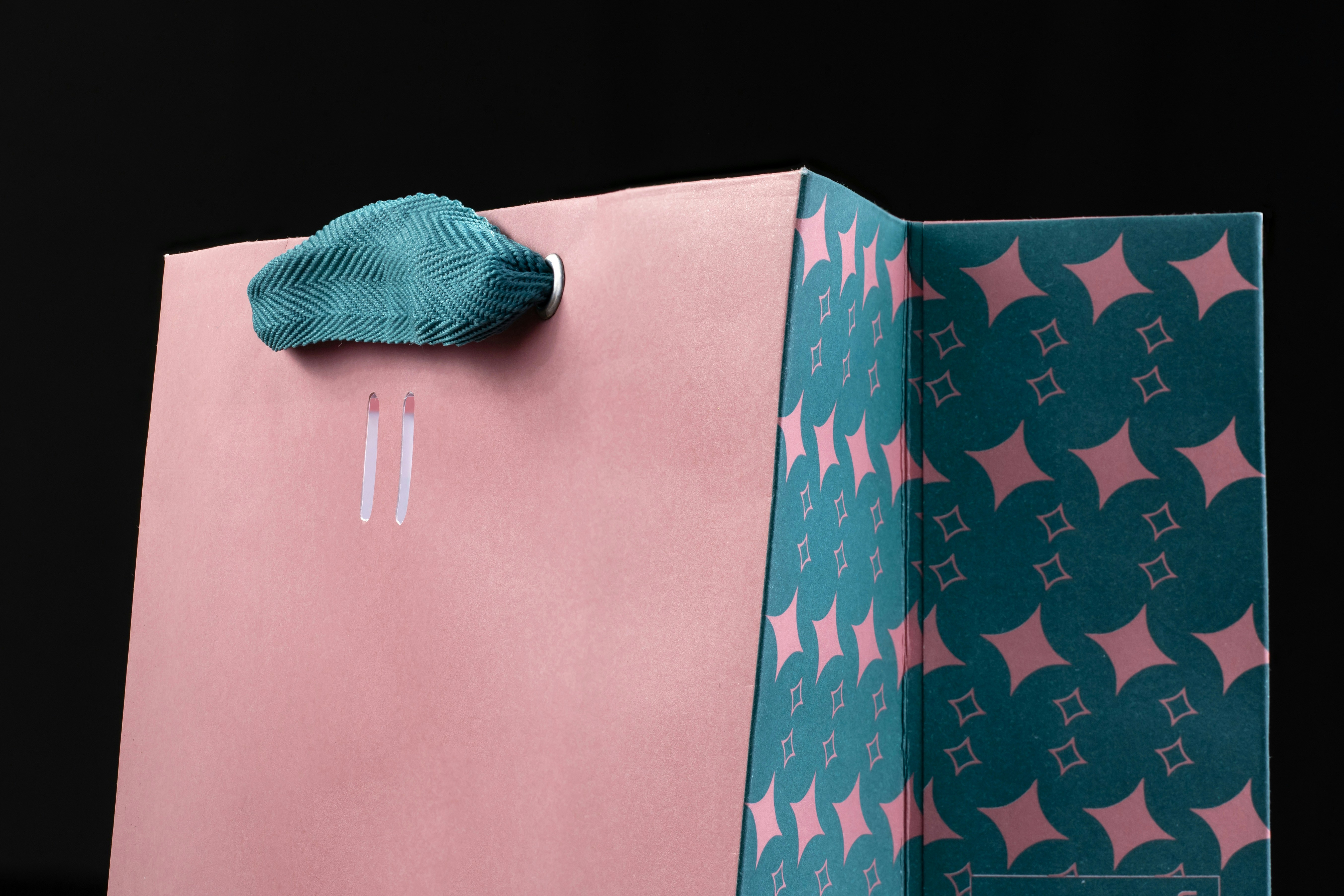 Pink and teal gift bag with a woven textile handle and decorative pattern against a black background.