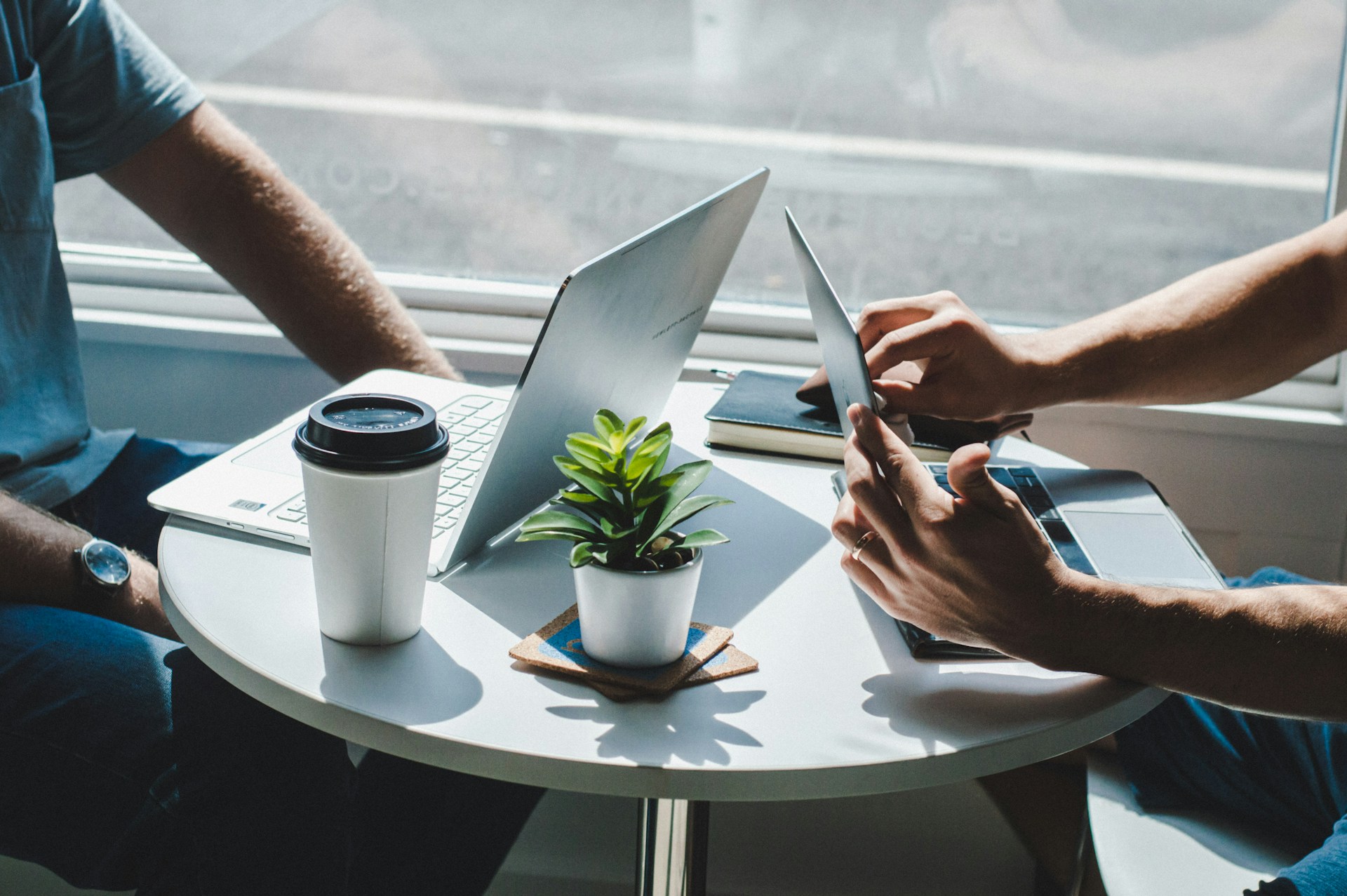 The photo presents two people working with laptops at a table.