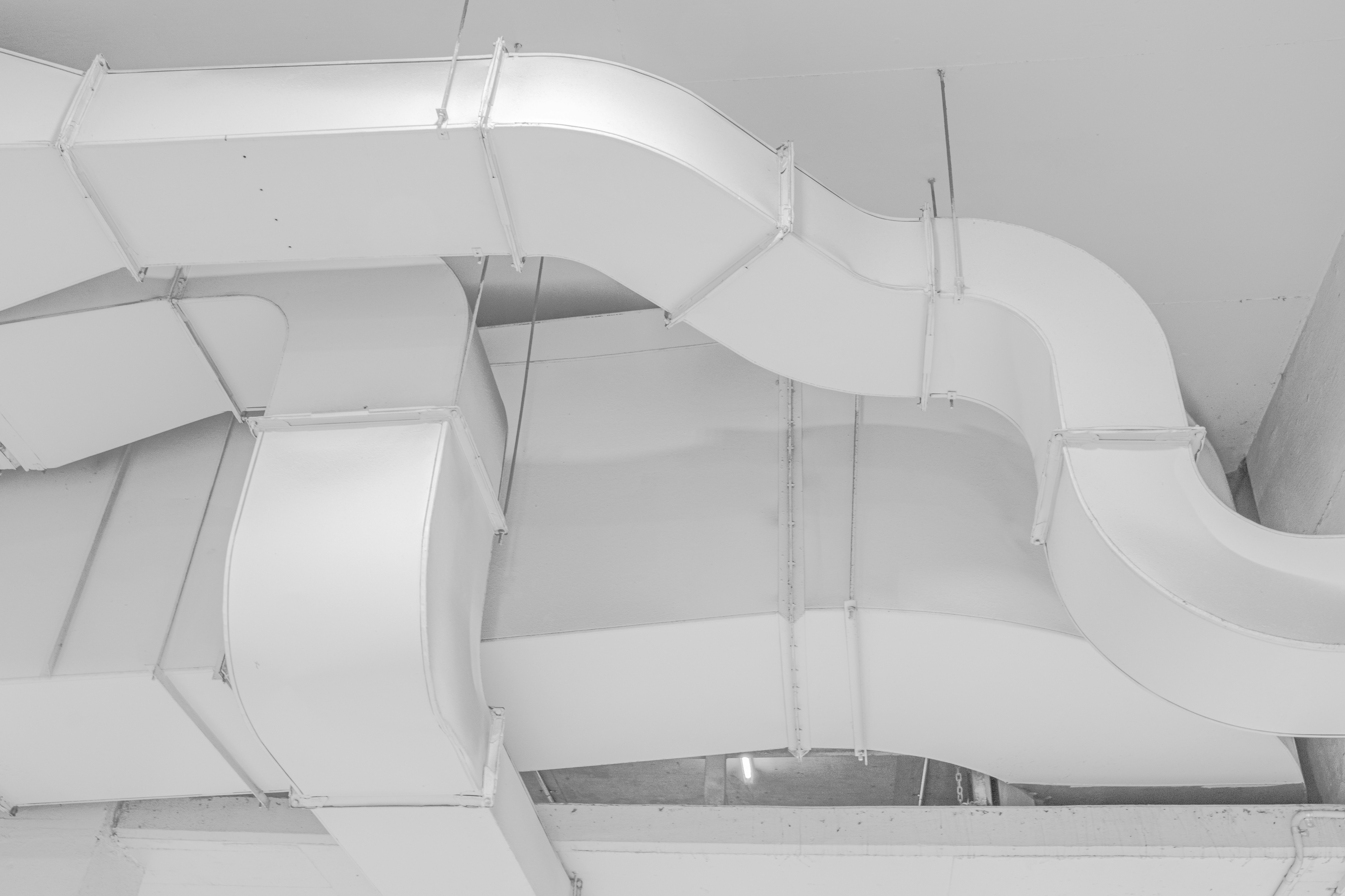 The picture presents large white ventilation ducts running across an industrial ceiling.