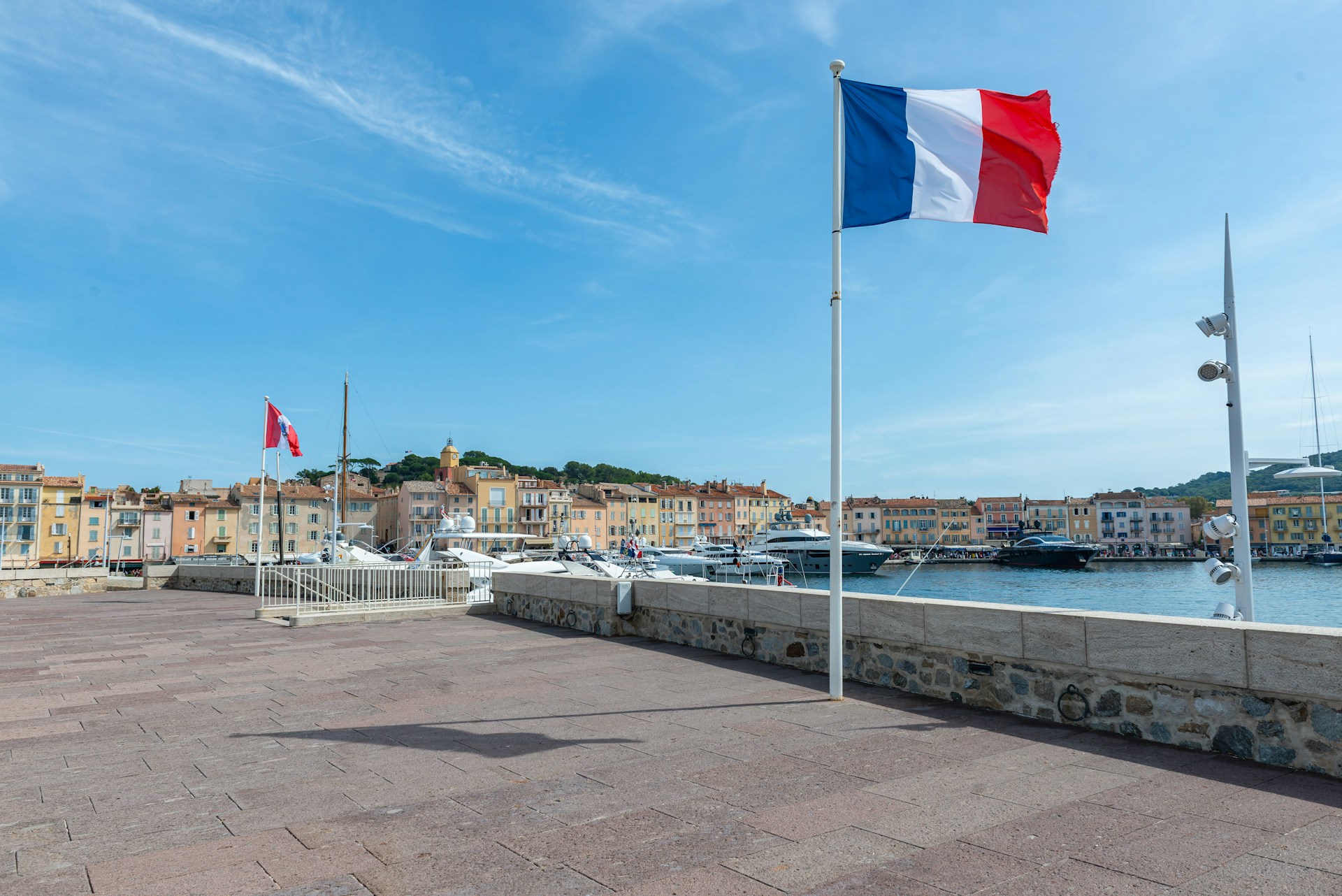 The photo presents a French flag flying over a marina with yachts and waterfront buildings in the background.
