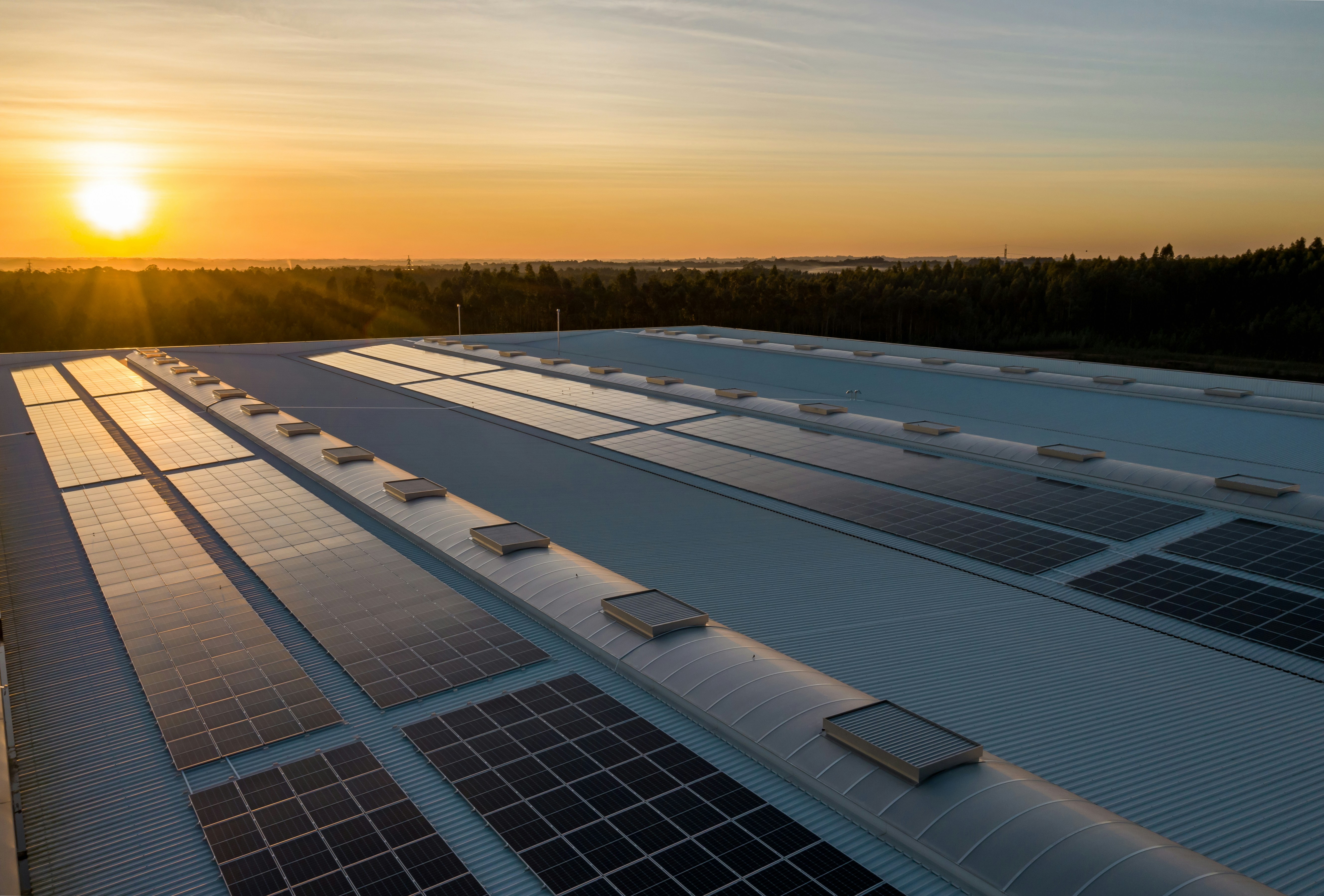 The photo presents solar panels on a large roof at sunset.