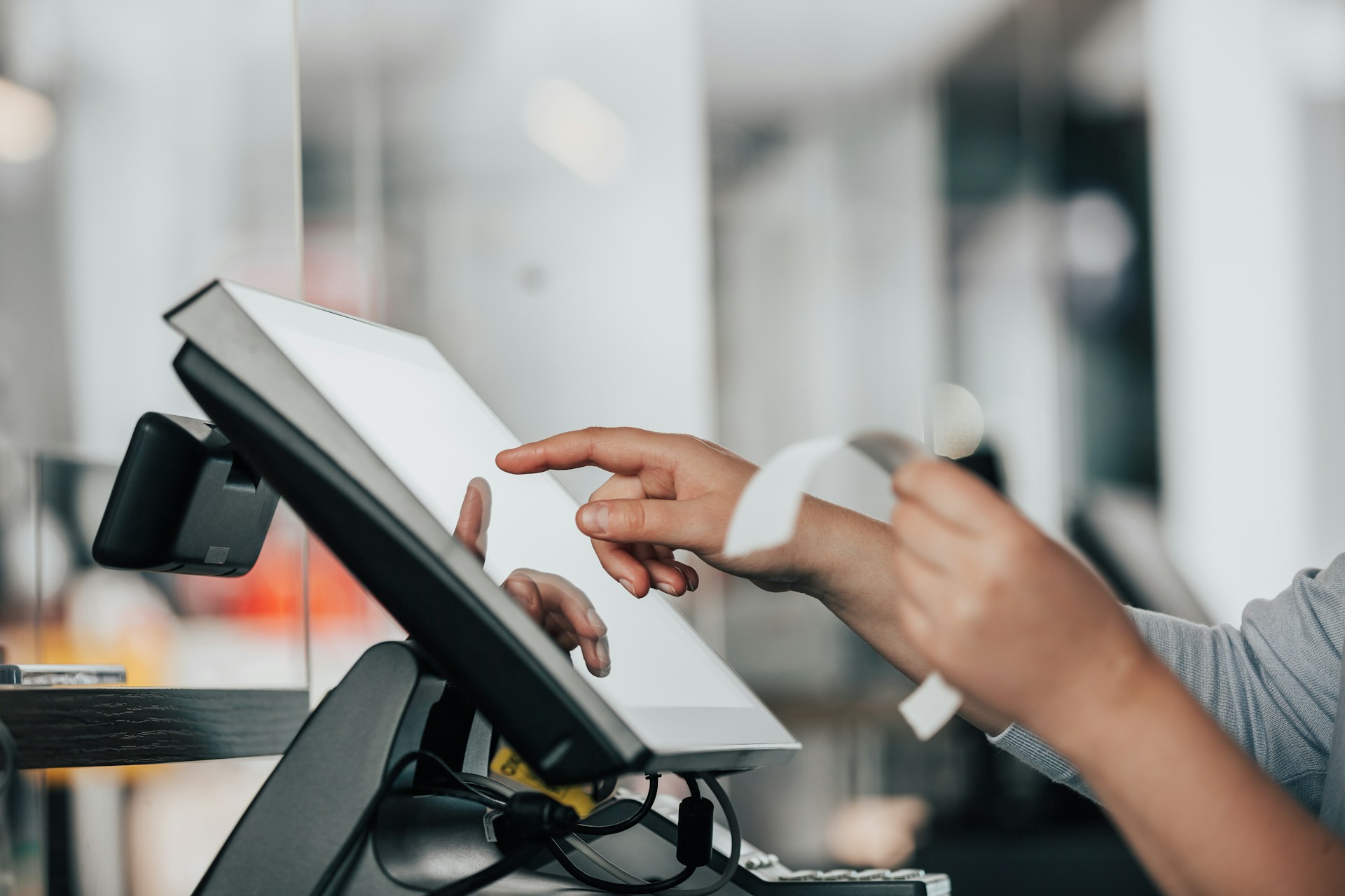 The photo presents a person using a touchscreen point-of-sale system while holding a receipt.
