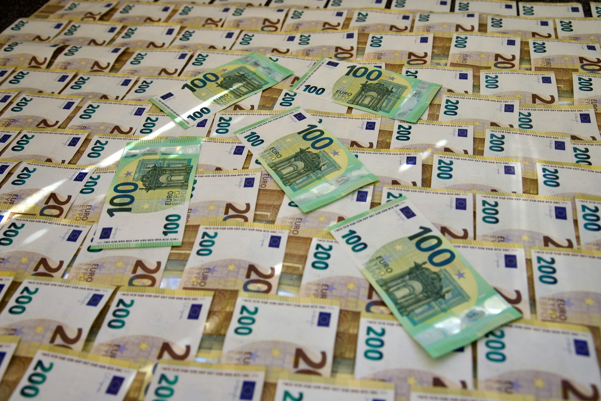 The photo presents stacks of €100 and €200 euro banknotes.