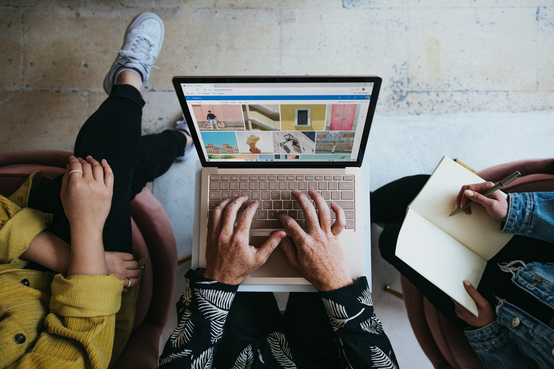 The photo presents people collaborating on a laptop while taking notes.