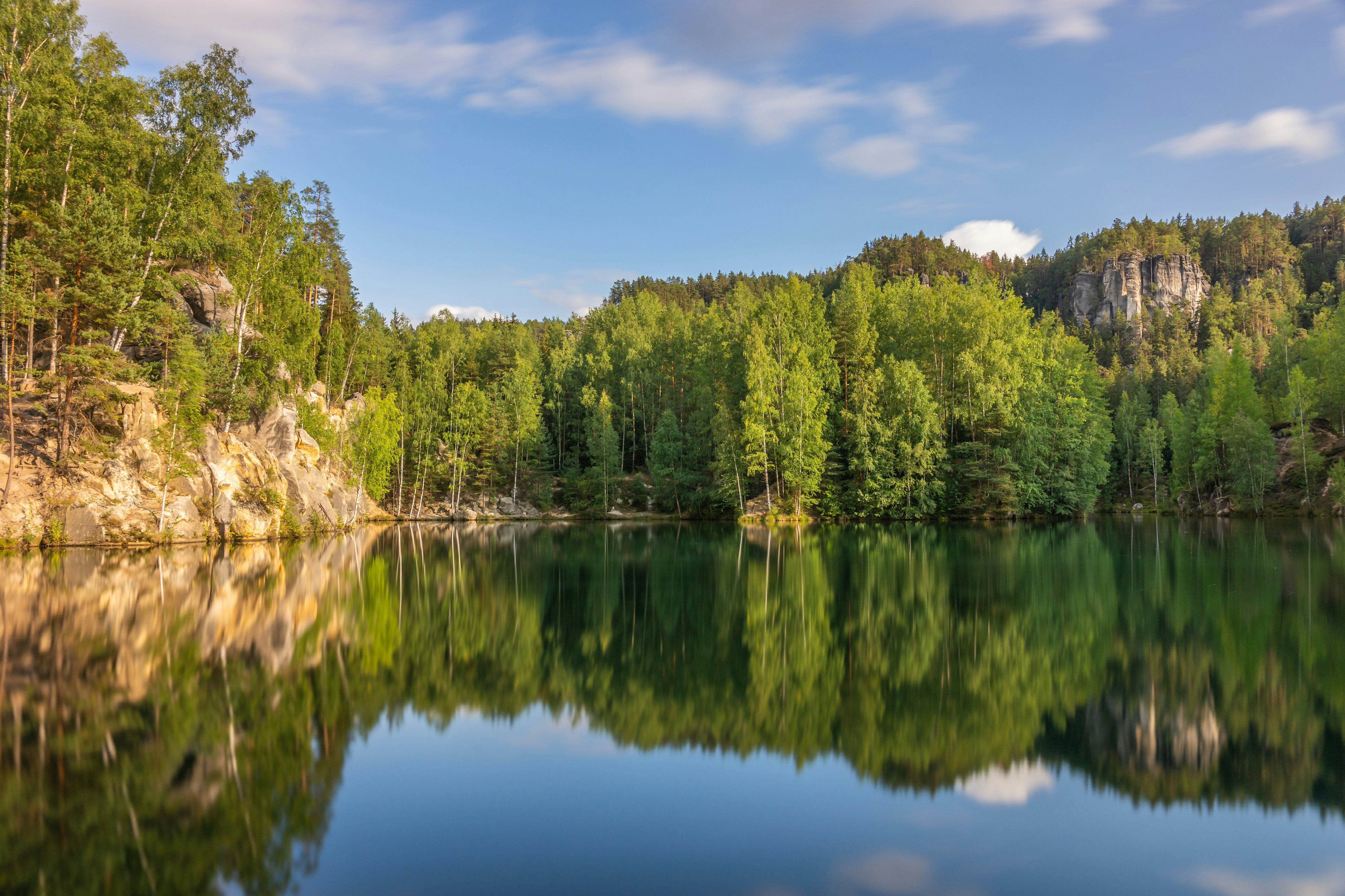 The photo presents a calm lake surrounded by a green forest.