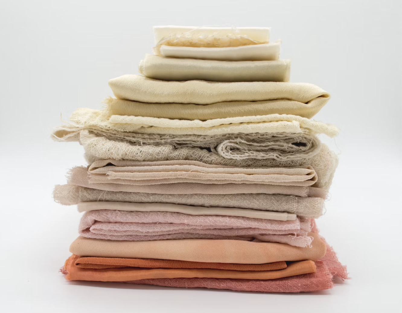 Stack of folded fabrics in pink, red, yellow, grey, and brown on a white surface. 