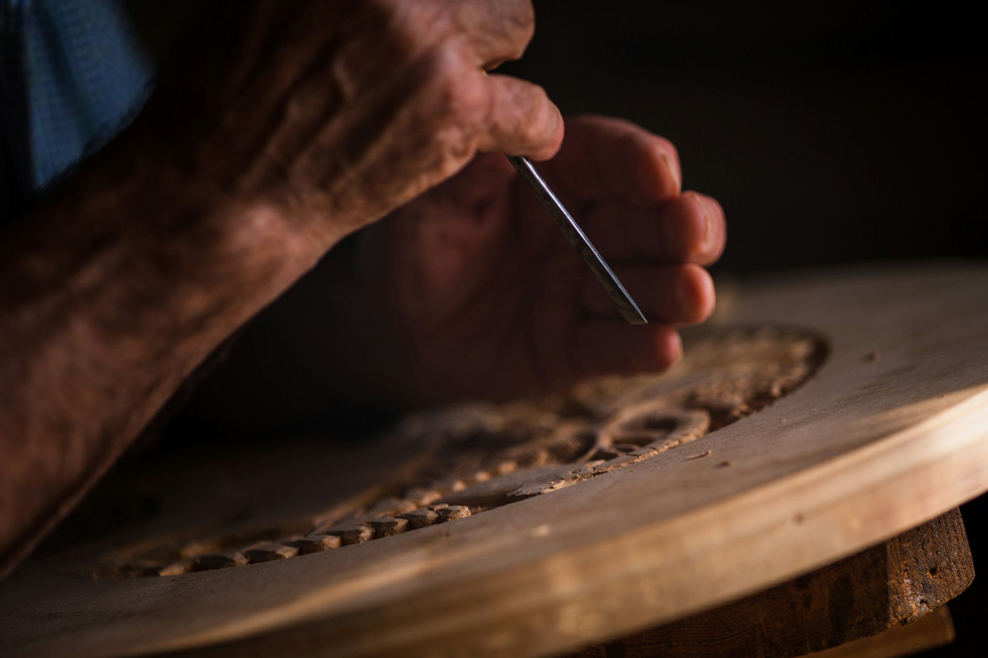 The photo presents a close-up of a person using a chisel to carve a decorative pattern into wood.