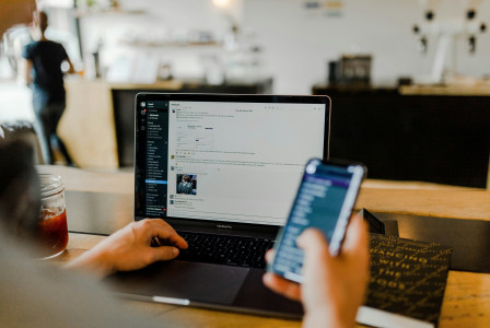 A photo presenting a person using a laptop and smartphone at a workspace