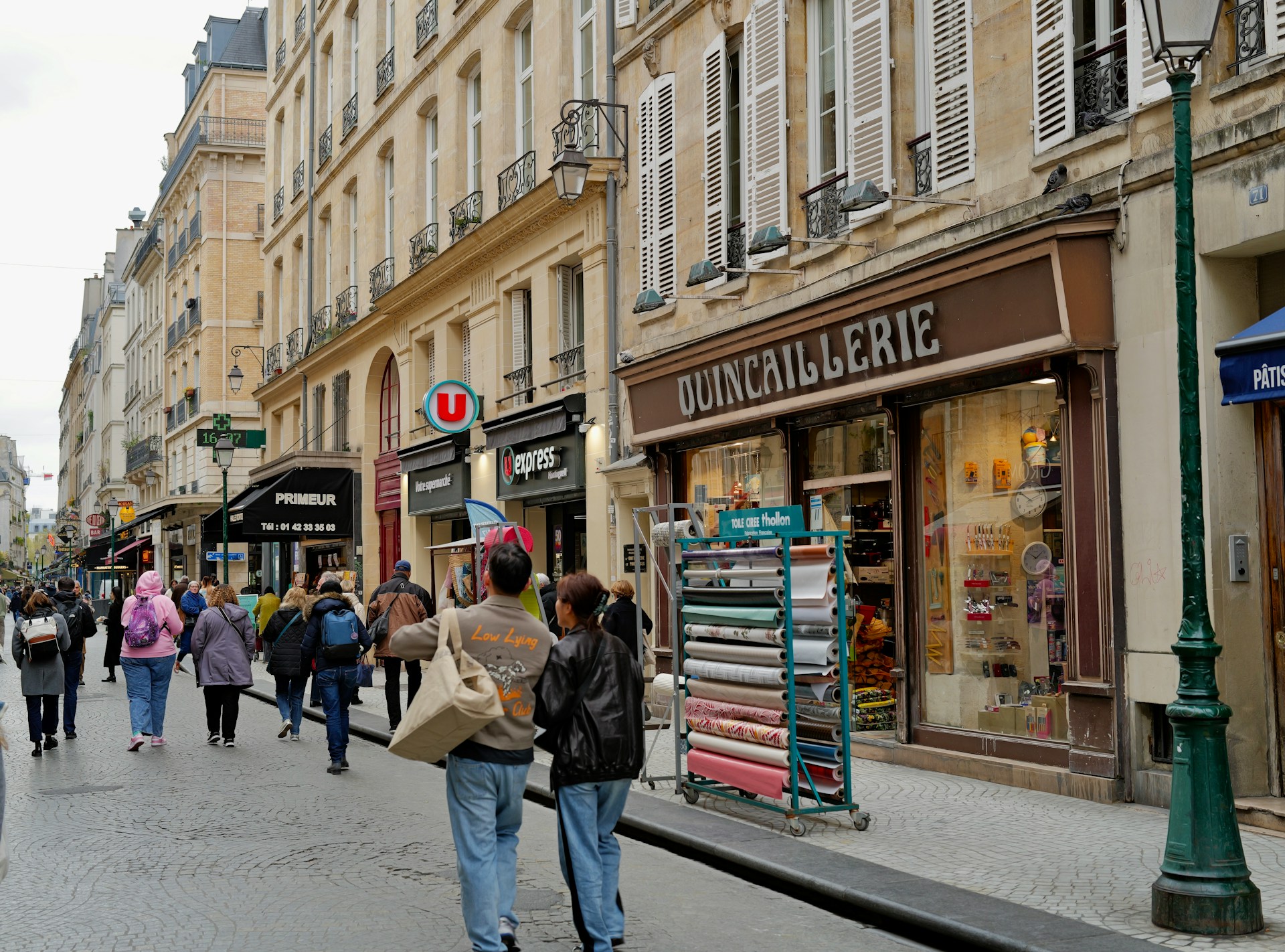 The photo presents a busy Parisian shopping street lined with historic buildings, cafés, shops and pedestrians.