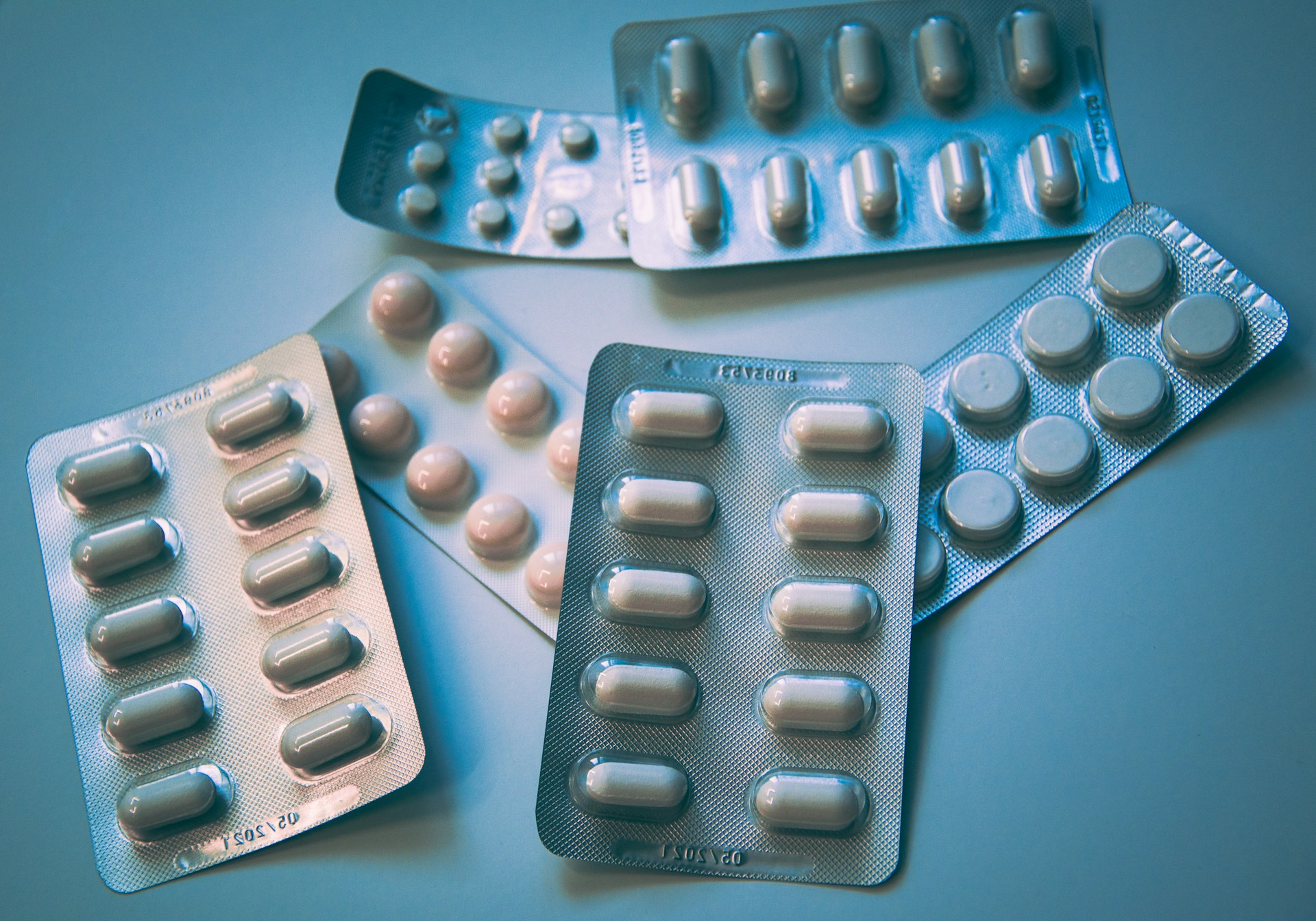 The photo presents several blister packs of assorted tablets and capsules arranged on a blue surface.
