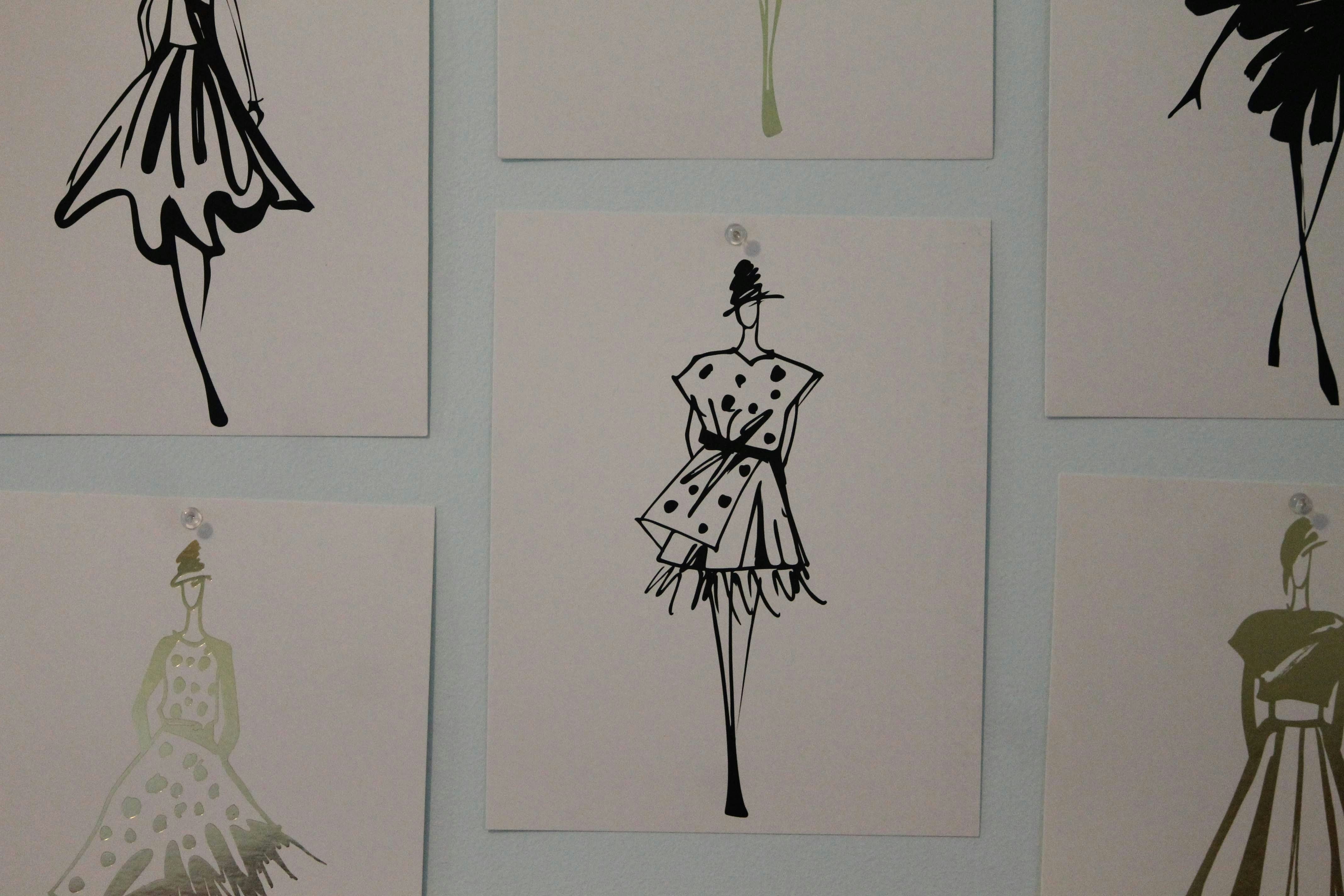 Fashion illustrations of dresses and outfits pinned to a wall, representing fashion design, creativity and collection development.