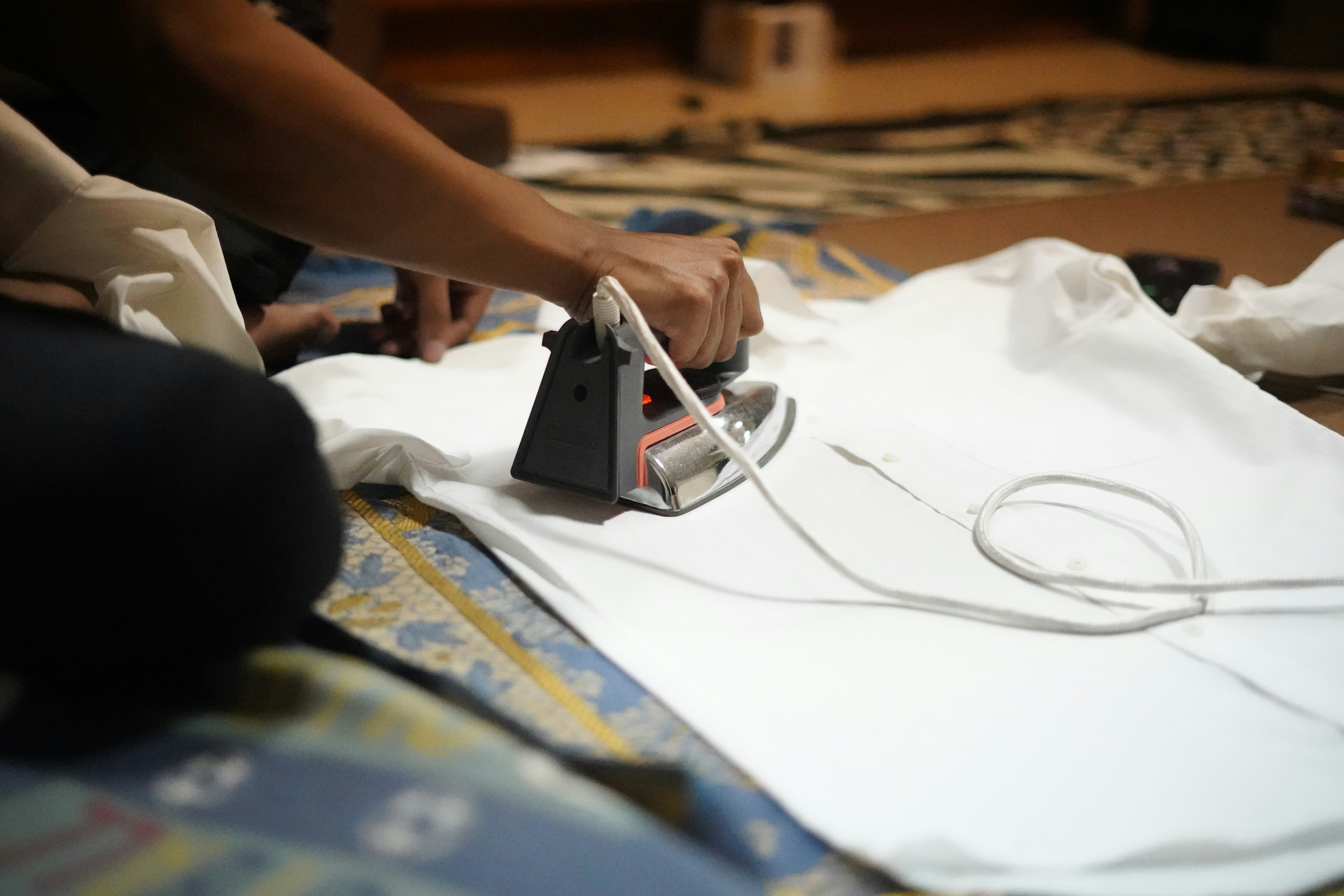 Person ironing a white shirt with a black iron, representing professional textile care, finishing and laundry services.