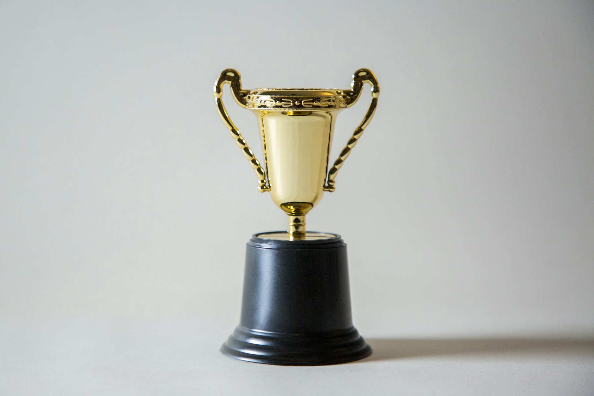 The photo presents a gold trophy cup with ornate handles on a black base, set against a plain light background.