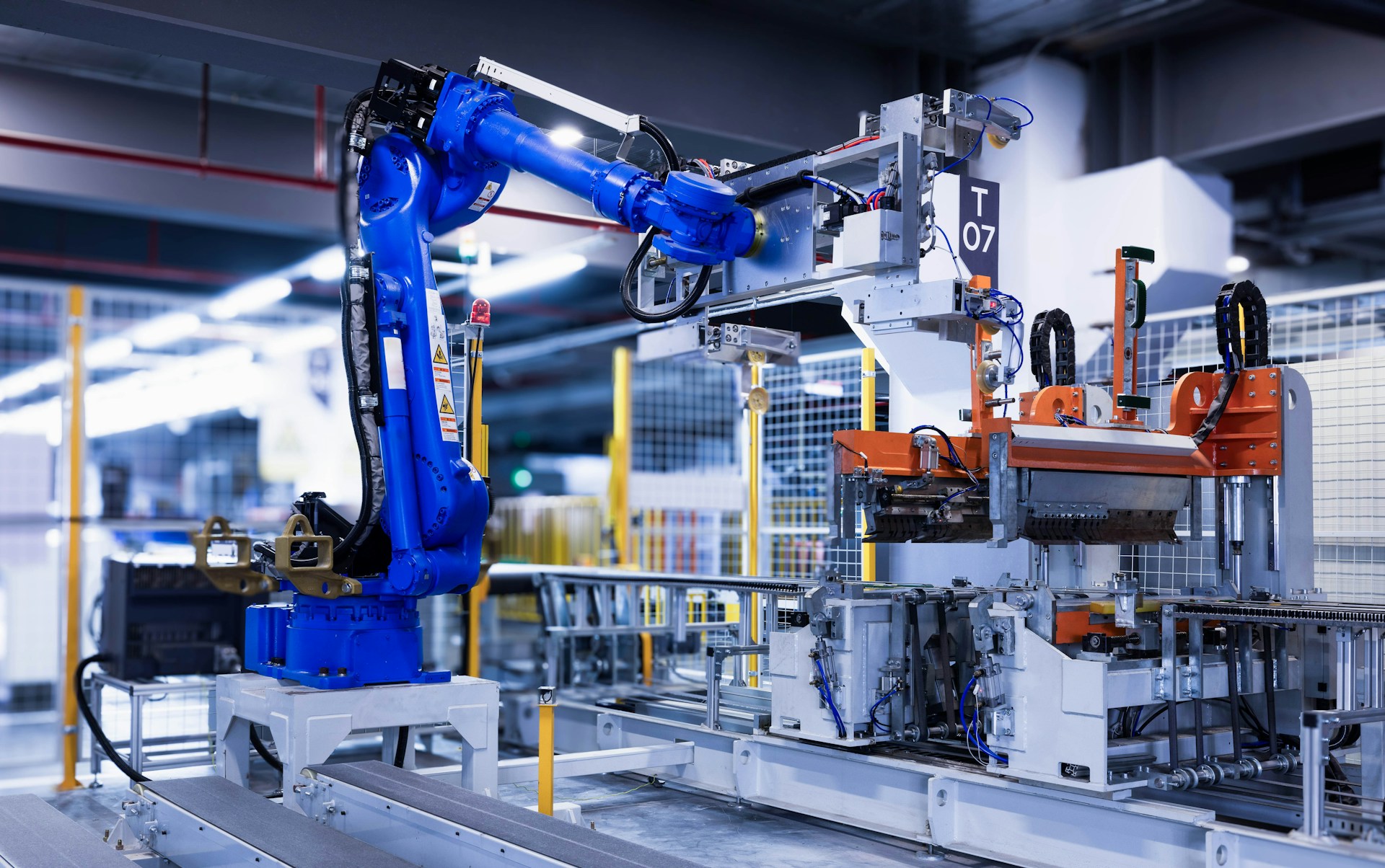 The photo presents a blue industrial robotic arm beside machinery and conveyor belts on an automated factory production line.