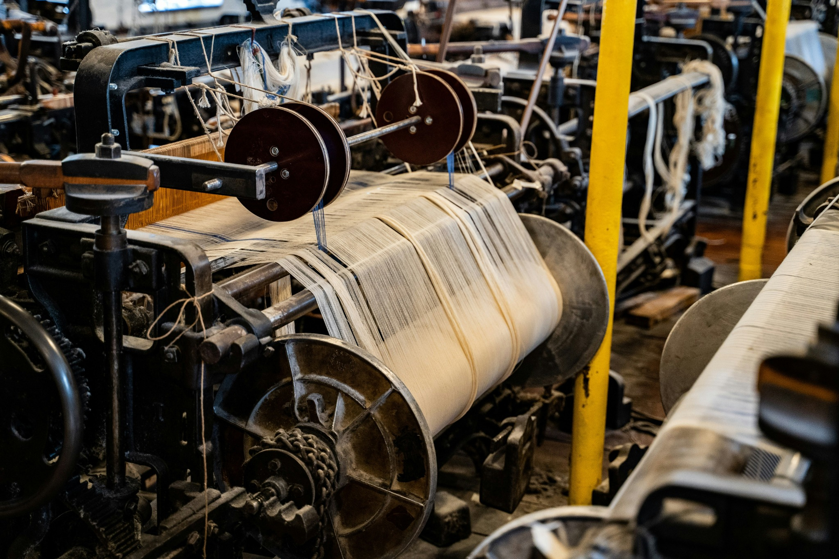 Industrial weaving machinery processing yarn in a textile production facility.