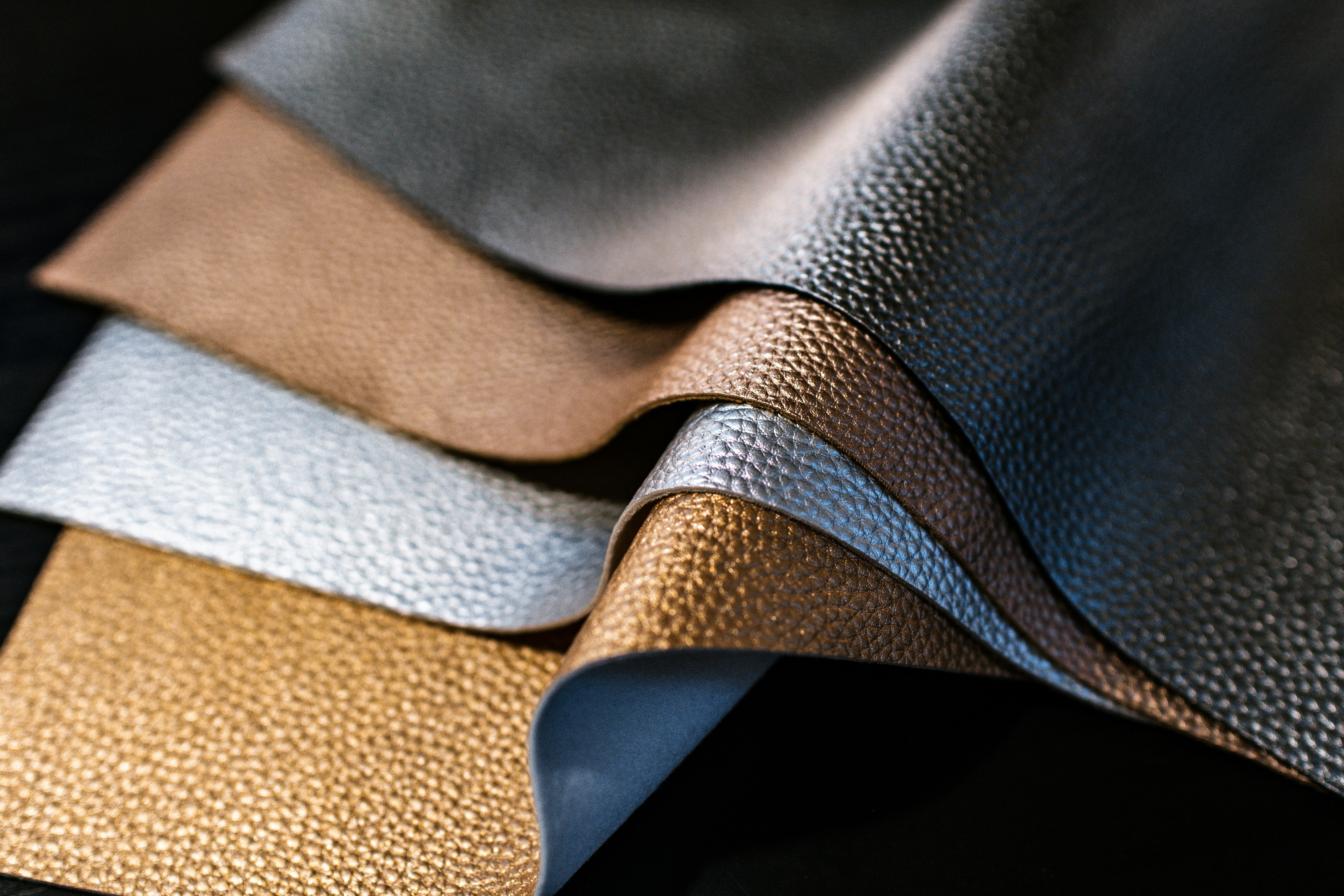 Close-up of layered textured material samples in metallic gold, silver, bronze and black tones, representing innovative material development and textile design.