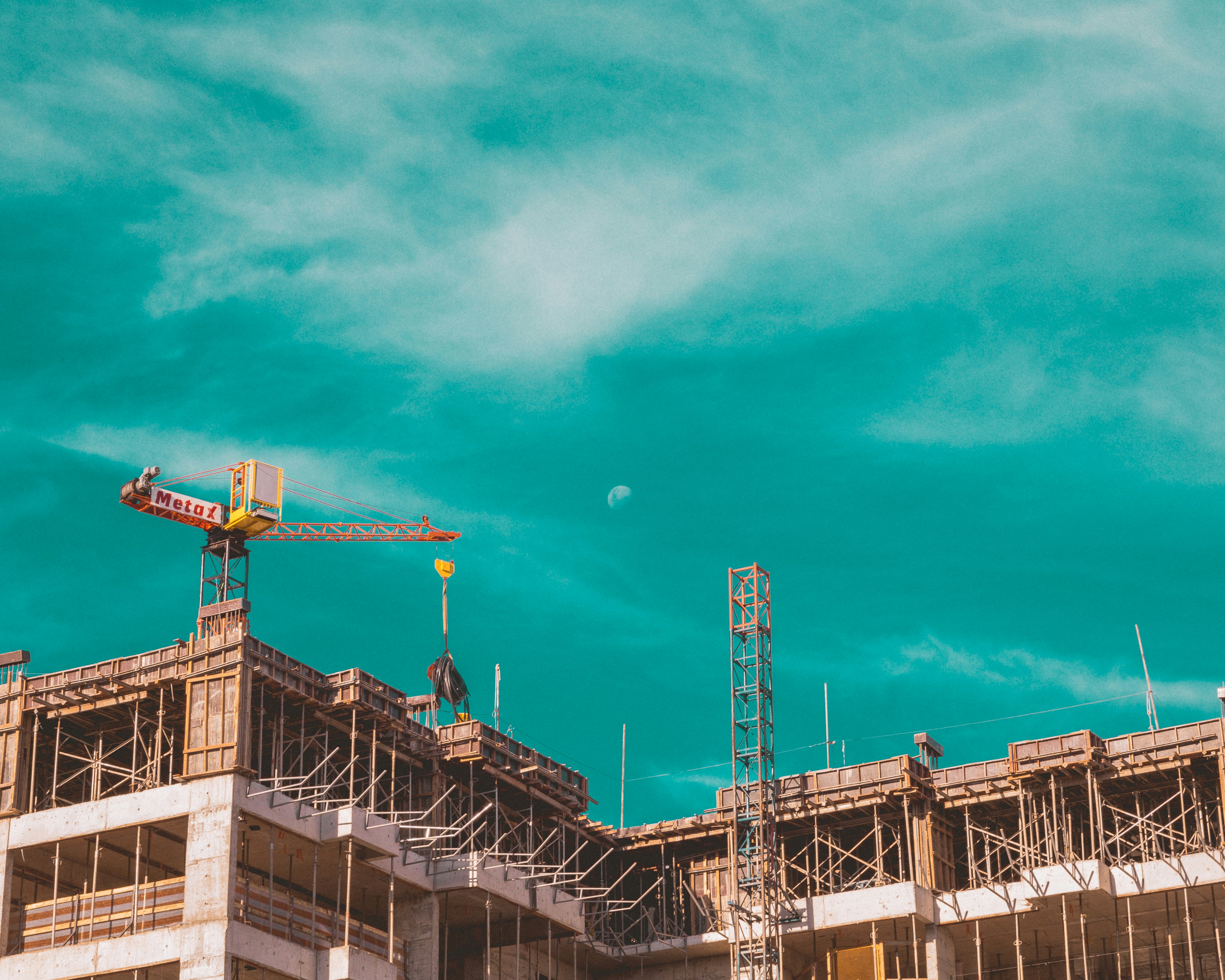This picture shows a building under construction, featuring exposed concrete floors, scaffolding, and a tower crane lifting materials.